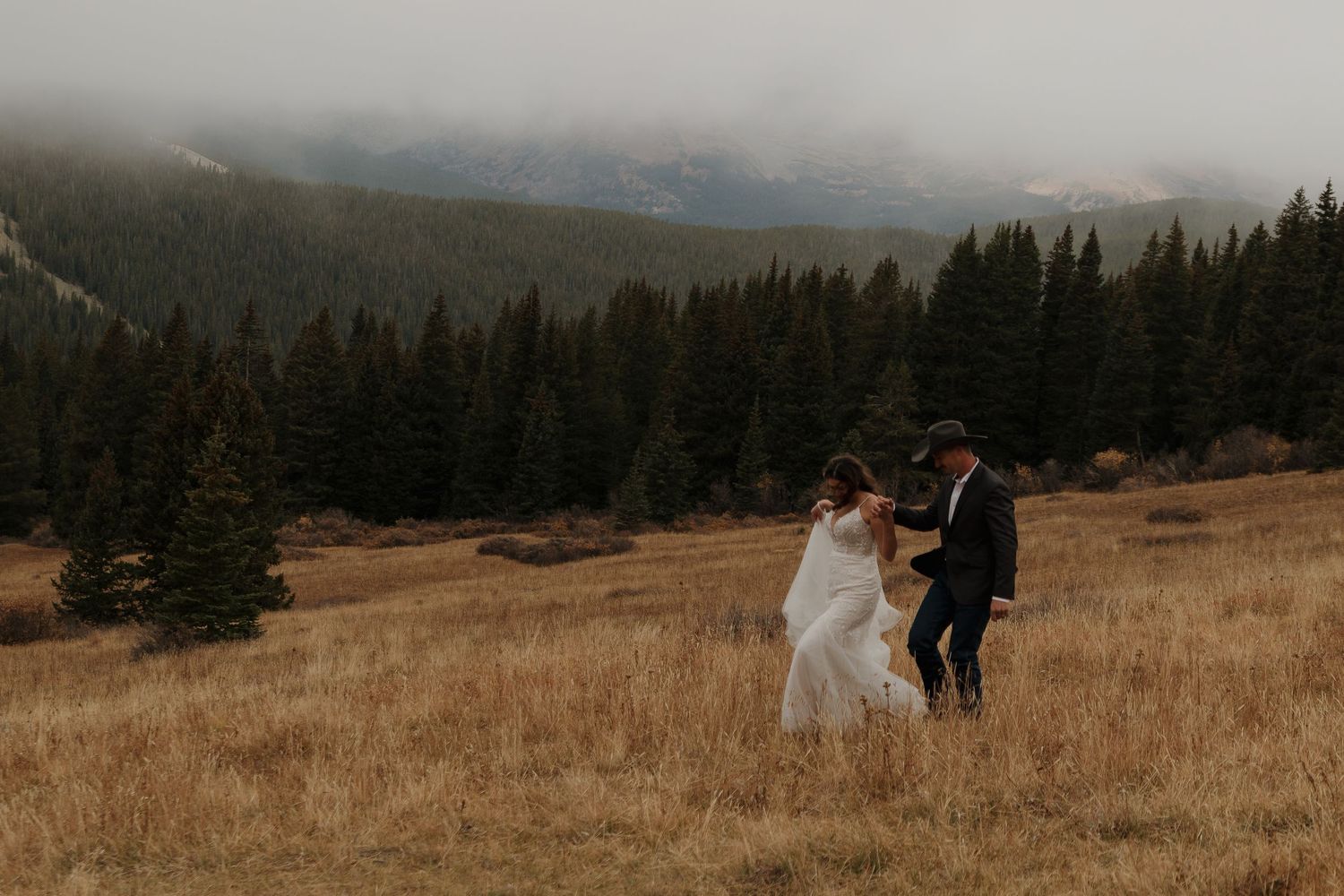 A couple shares a tender moment in a golden mountain meadow surrounded by evergreen forest.