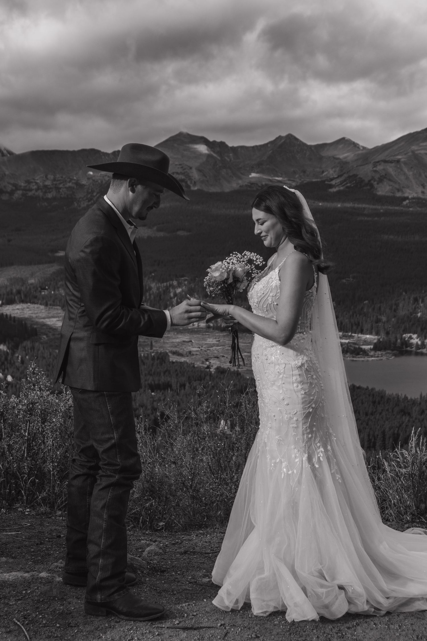 A dramatic black and white wedding photoshoot with mountain vistas and cloudy skies as backdrop.