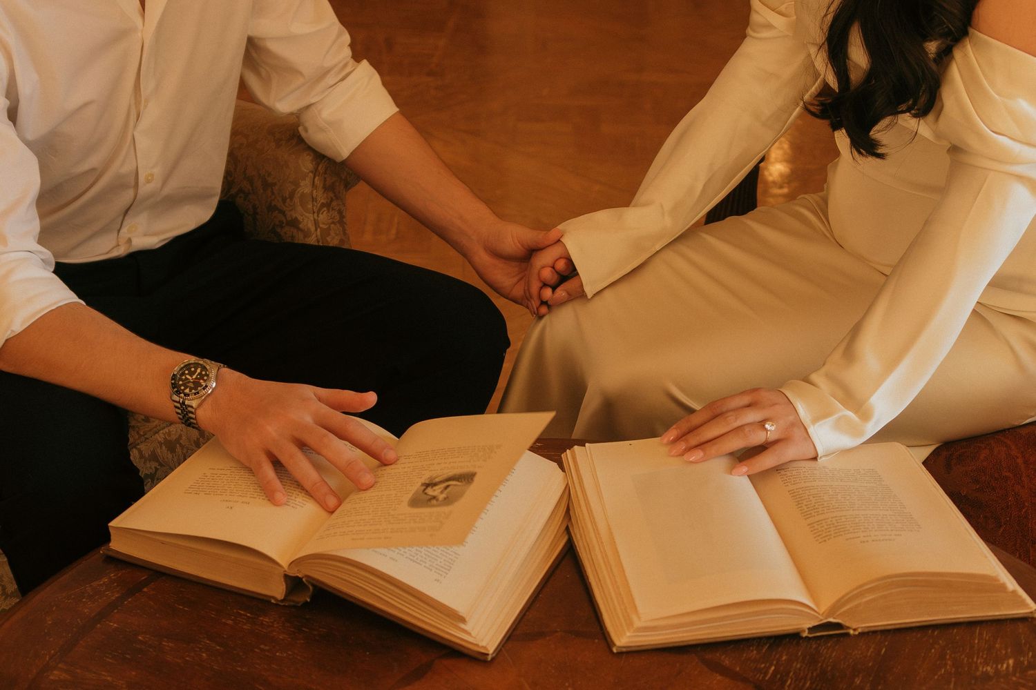 Students sitting at wooden tables study together with open books and papers spread out in a library setting.