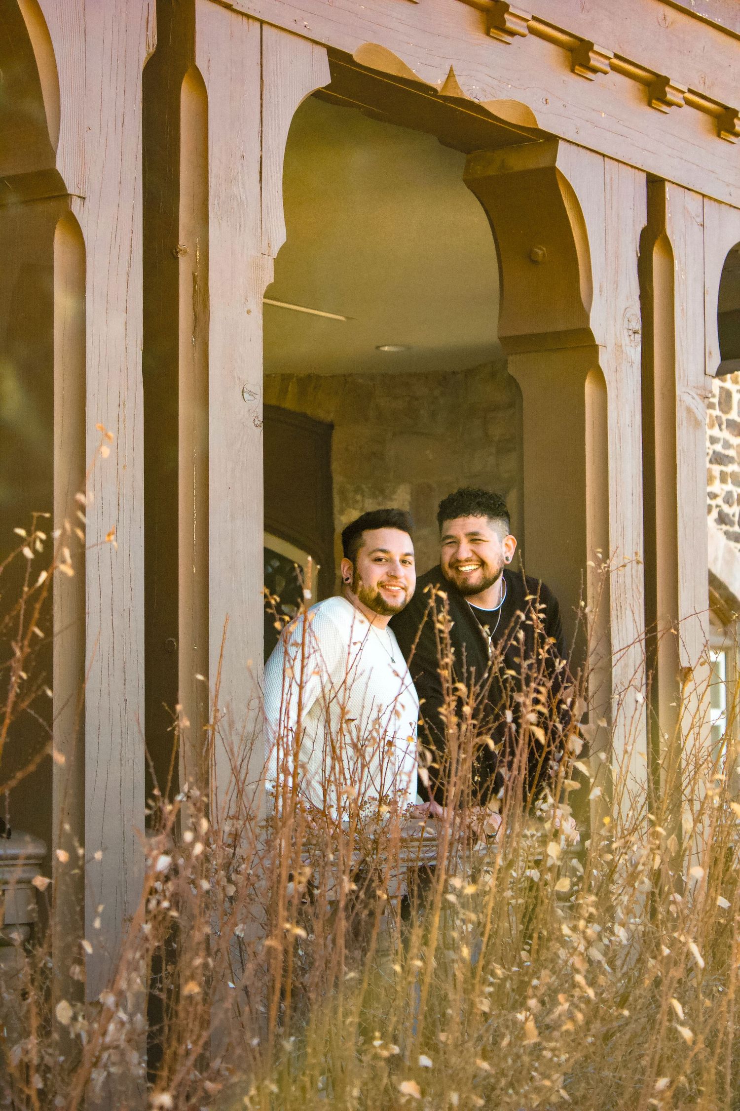 Couple sharing a tender moment framed by ornate stone archways with dried grass in the foreground.