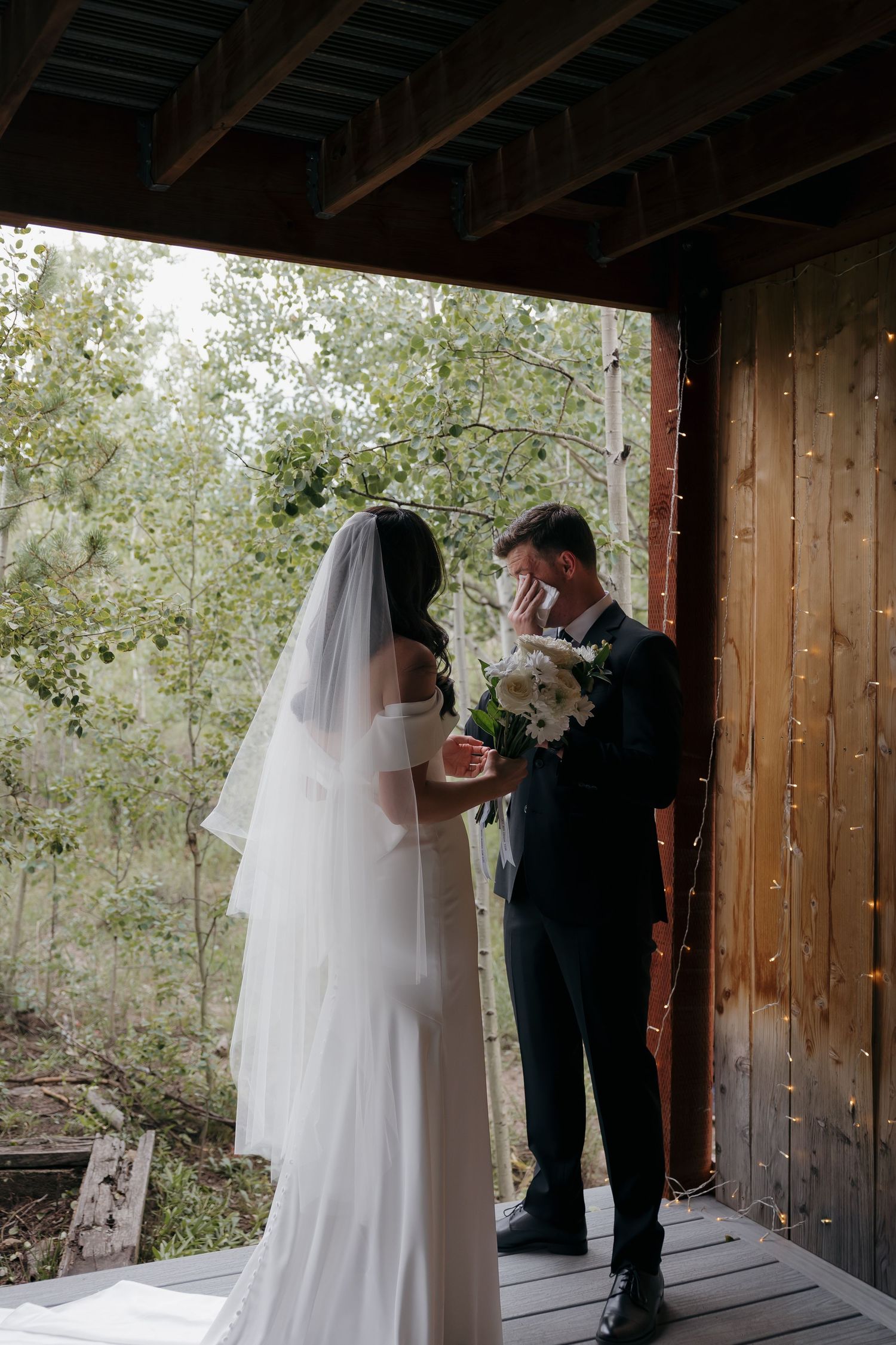 Emotional groom covering his mouth in tears during first look with bride in white wedding gown.