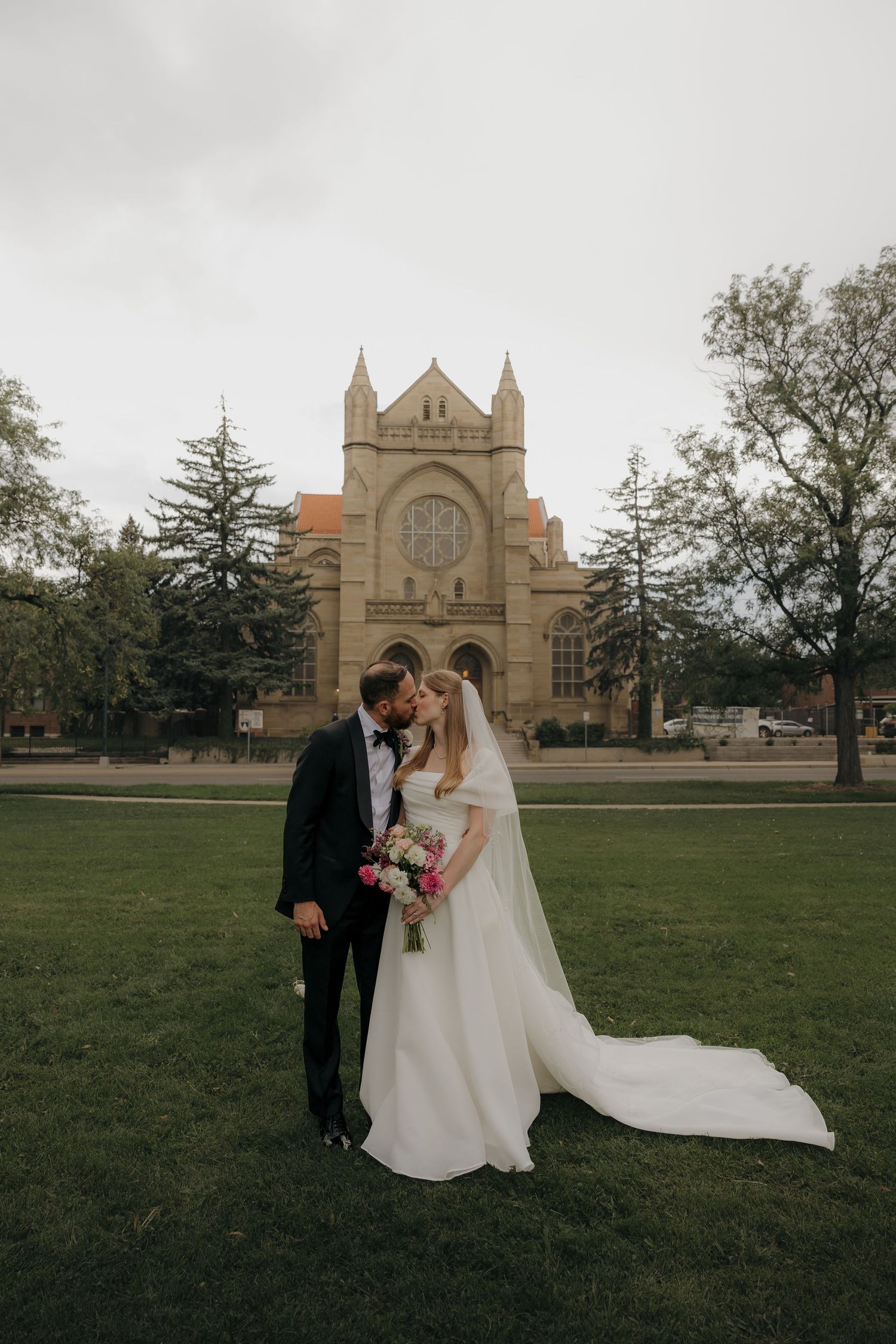 Bride and groom share romantic moment on lawn in front of historic stone church on their wedding day.