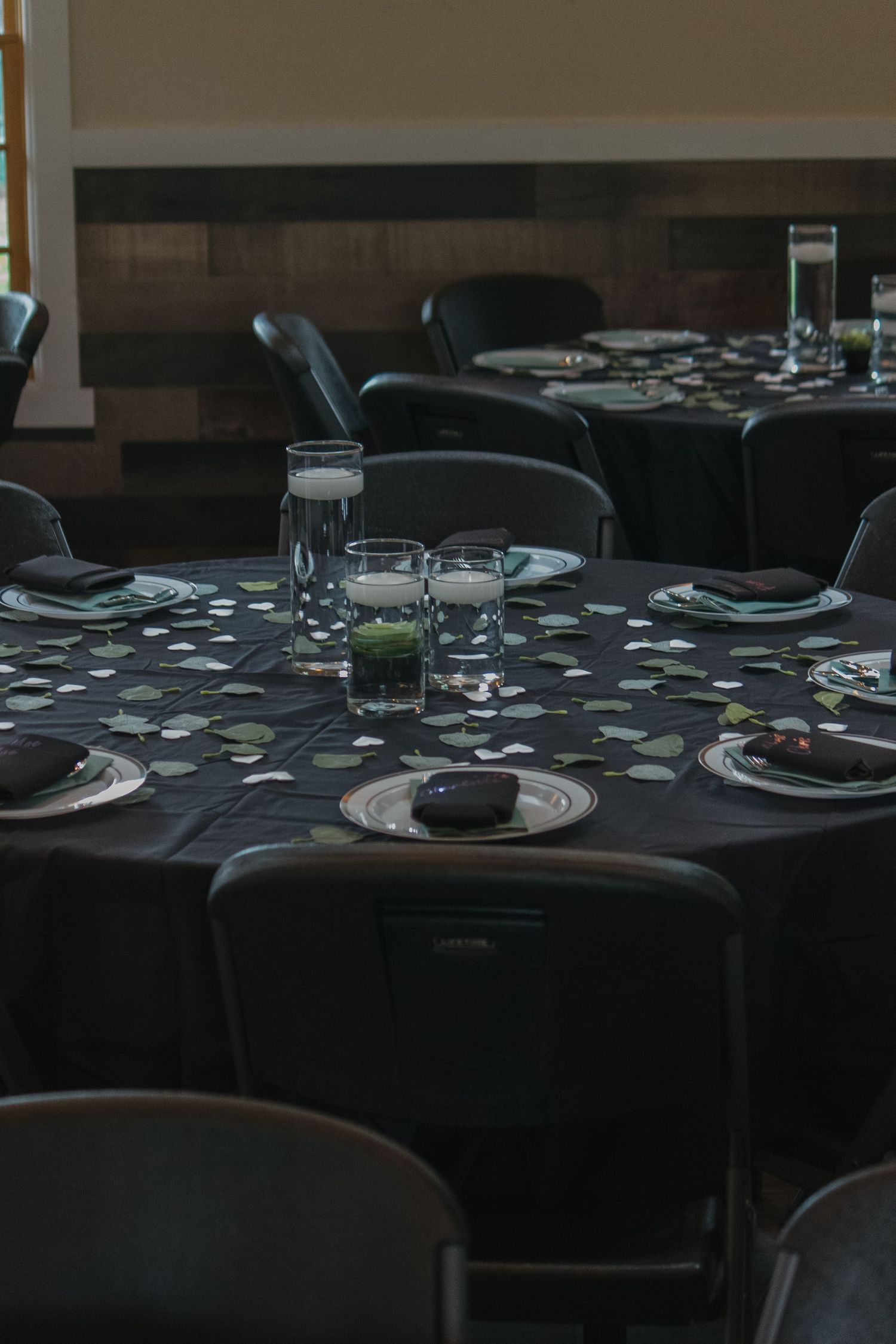 Elegantly set dining tables in a dark room with white linens and formal place settings for a special occasion.