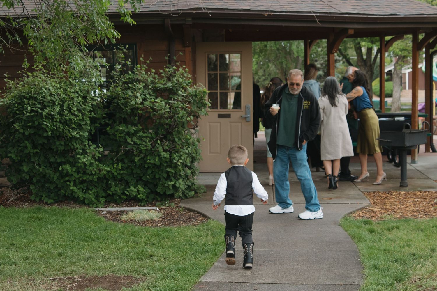 A young child walks along a garden path toward wedding guests.