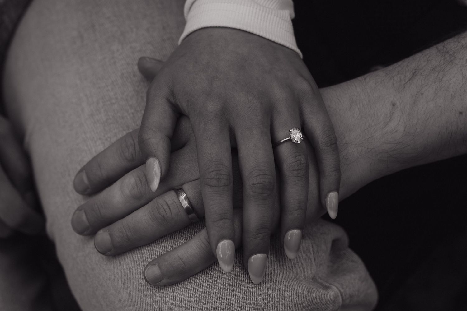 Black and white close-up of hands with wedding rings resting together.