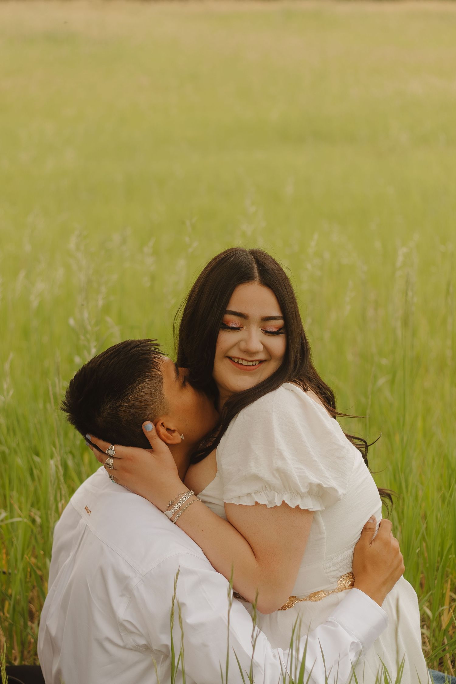 Joyful couple sharing a romantic embrace in a sun-drenched field of tall grass.