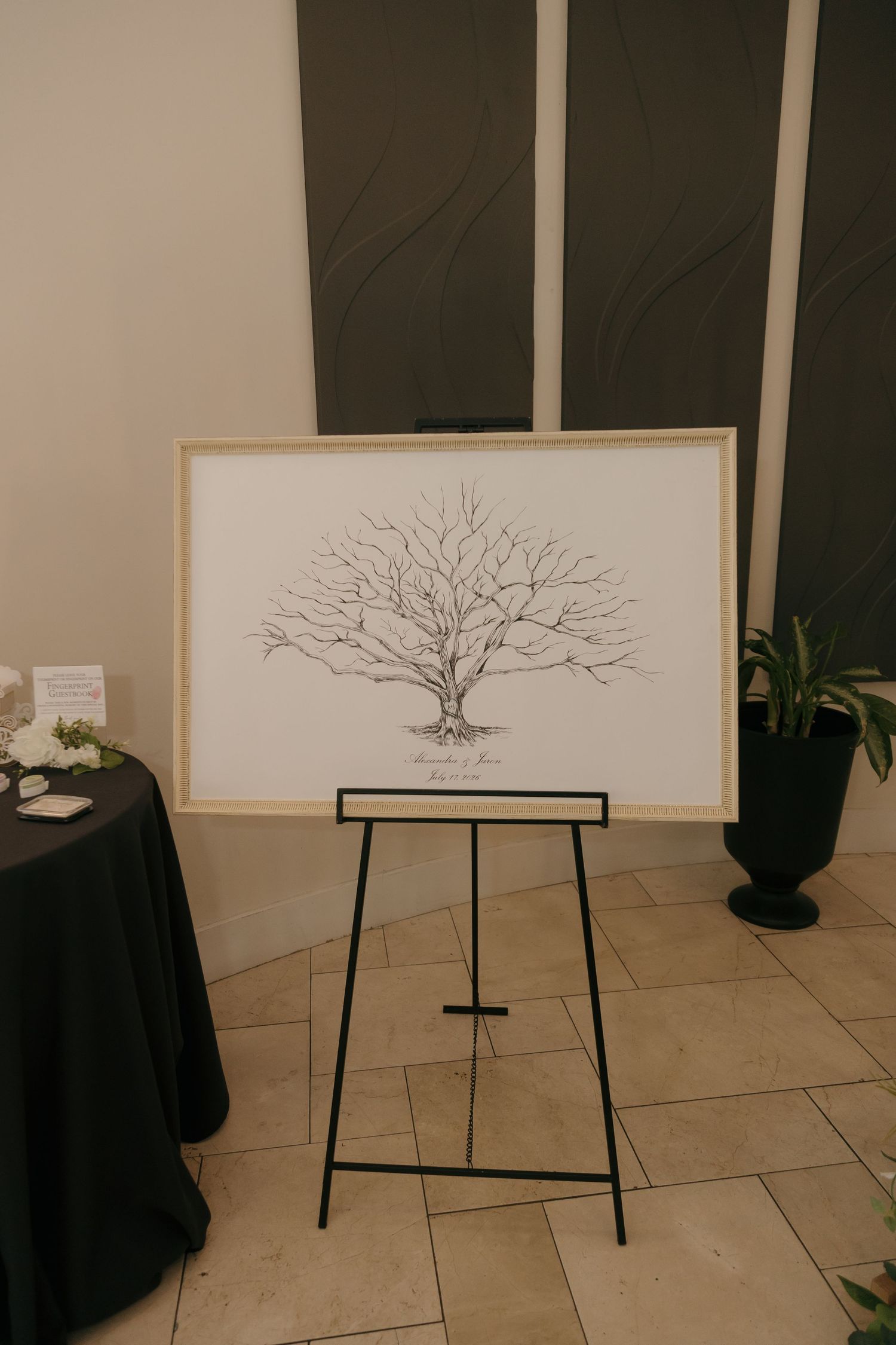 Elegant wedding fingerprint tree guest book display on a black easel in a modern venue.