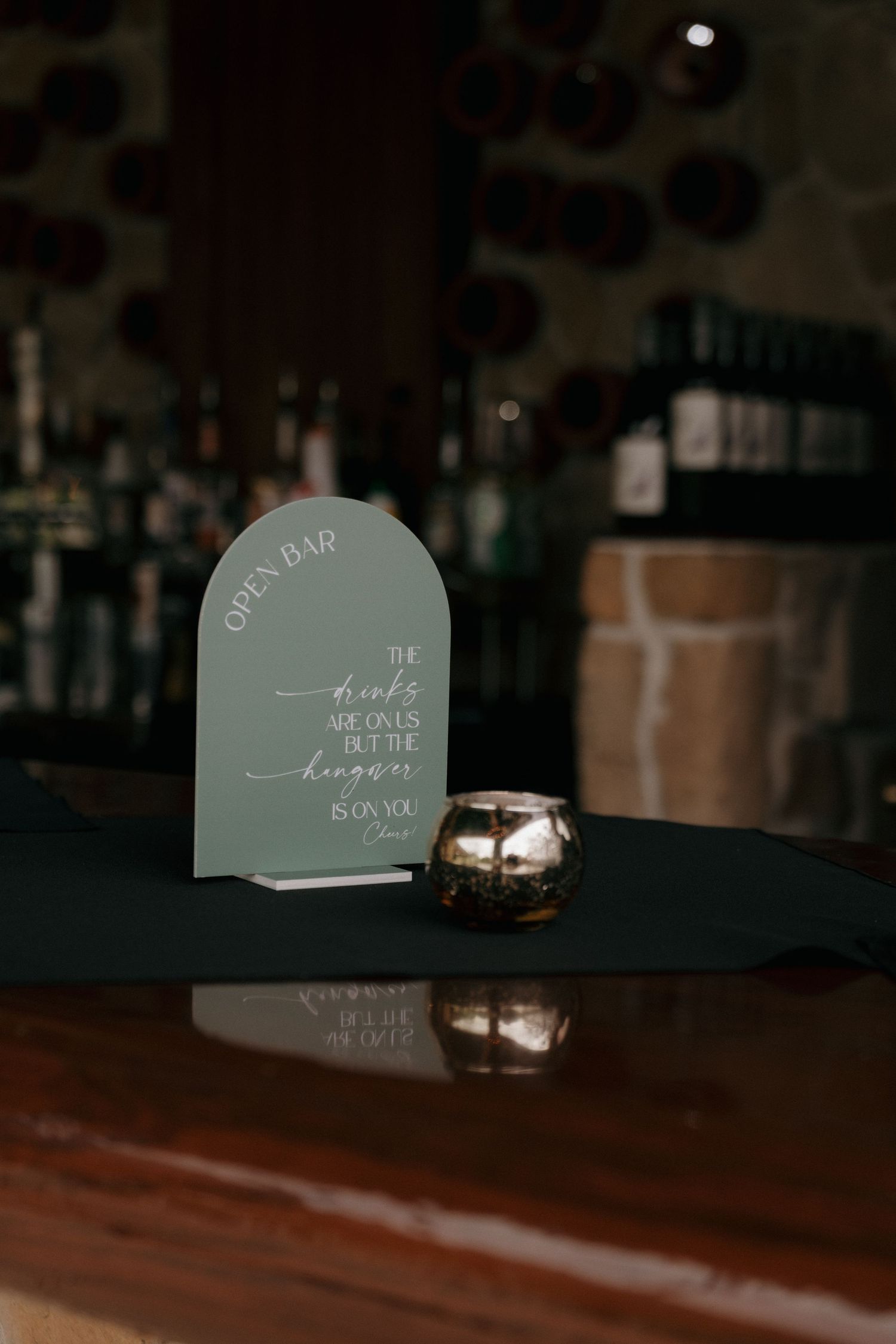 Sage green arched open bar sign with elegant calligraphy script on dark wood bar counter at wedding reception.