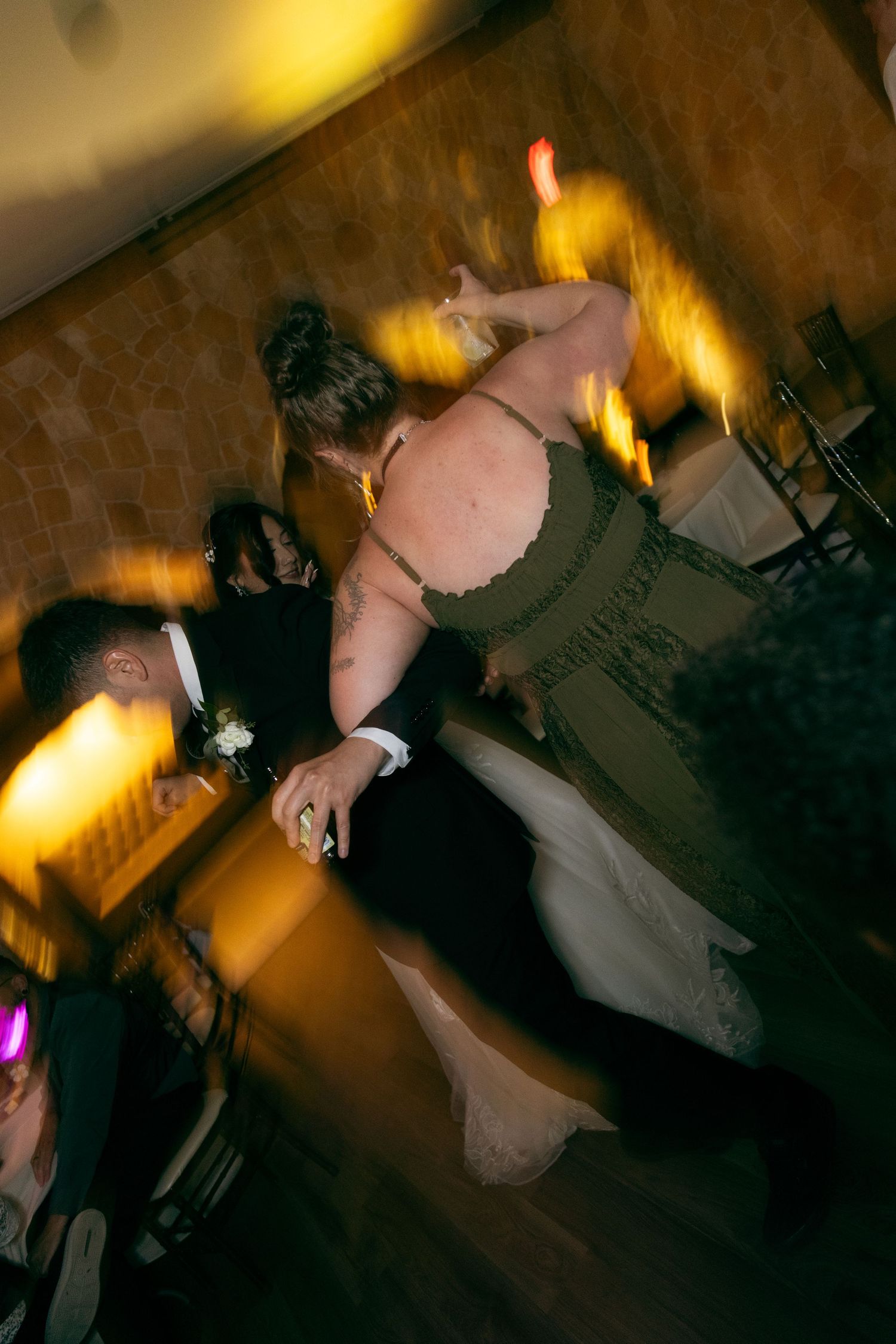 Motion blur photo of guests dancing energetically with glowsticks at lively wedding reception.