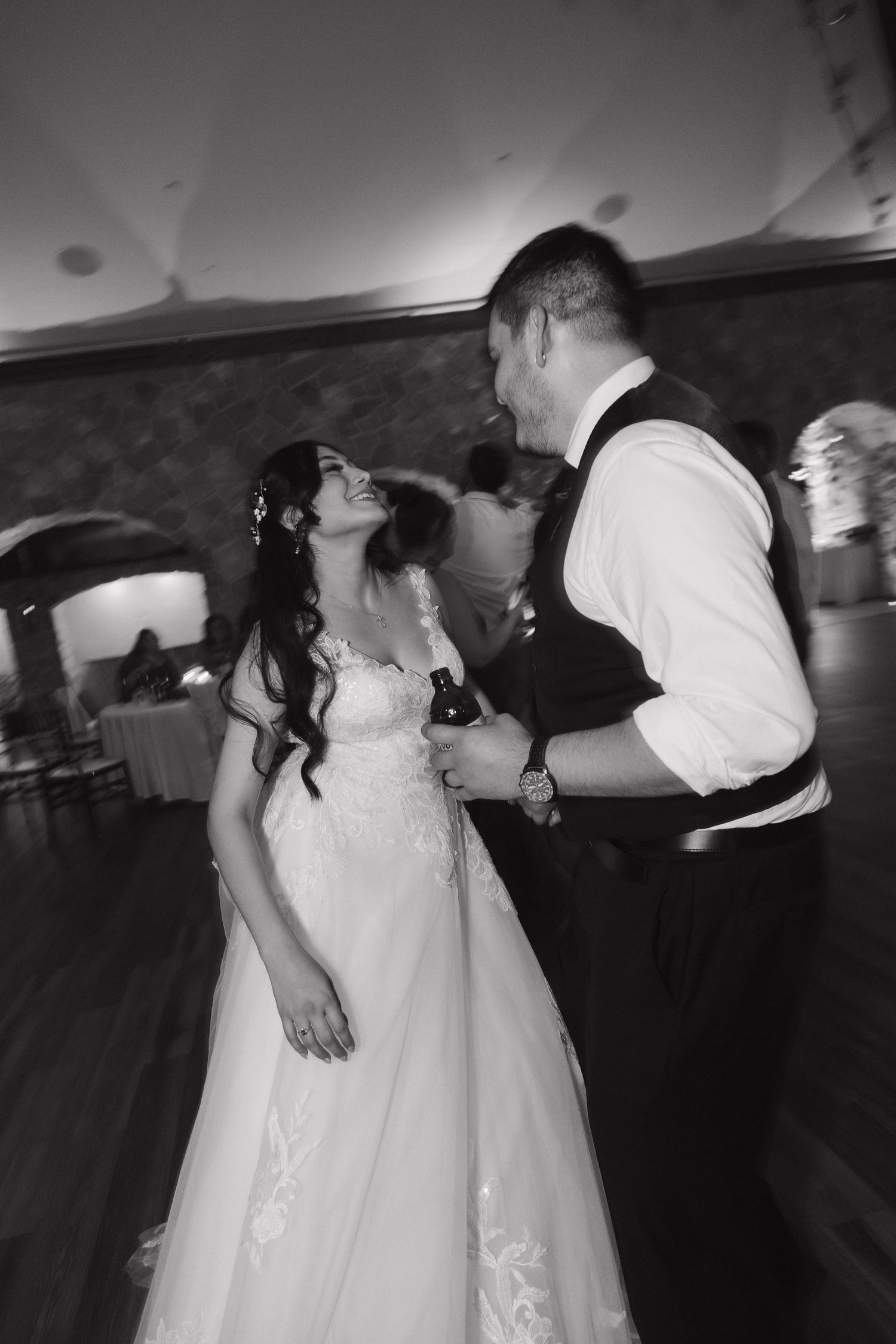 Bride and groom share romantic first dance, gazing at each other during black and white wedding reception.