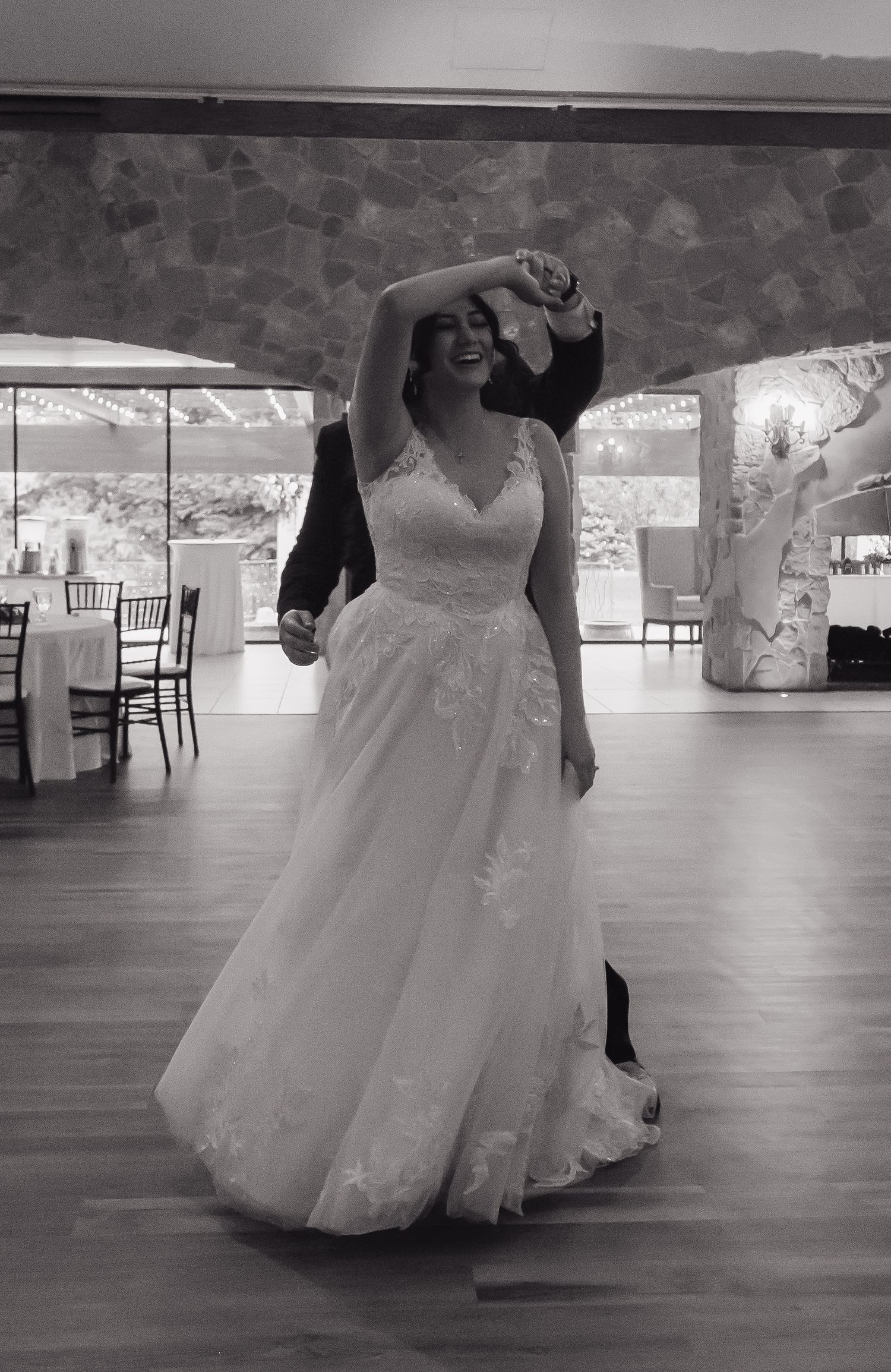 Black and white photo of bride in lace gown being twirled during first dance.