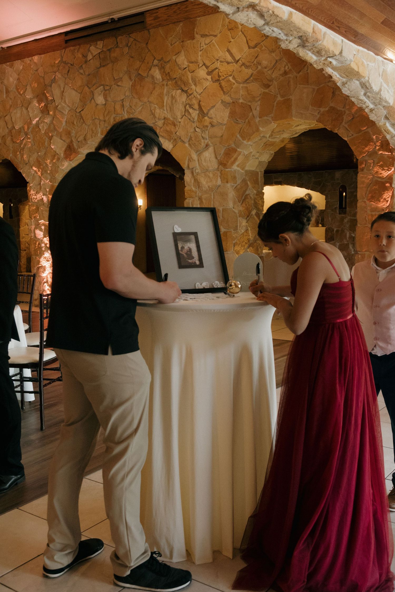 Guests signing a framed photo at a wedding reception in a rustic stone venue.