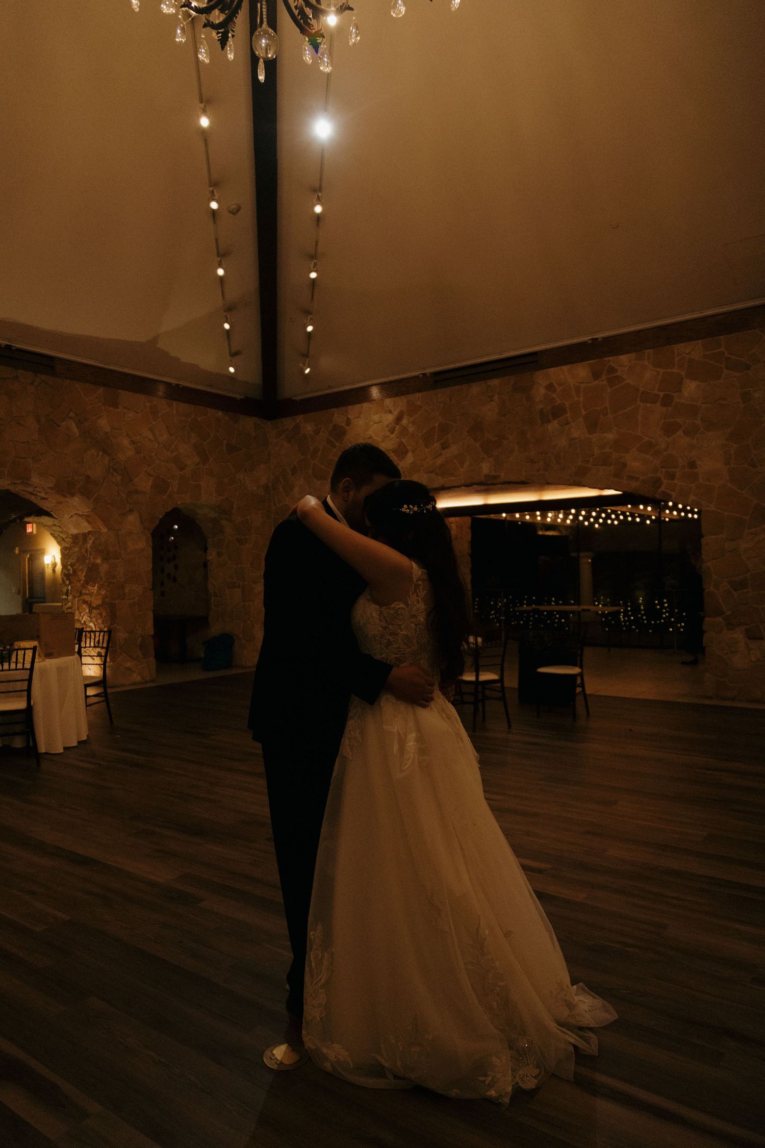 Bride and groom sharing intimate first dance under soft string lights in a romantic rustic venue.