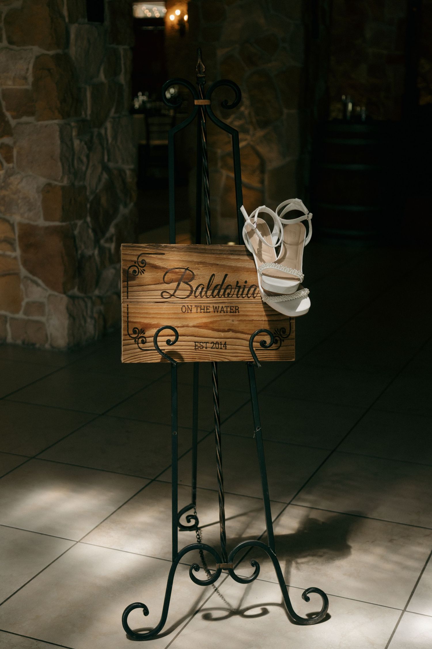 Rustic wooden wedding sign on ornate black easel with white bridal heels displayed at Baldoria on the Water venue.