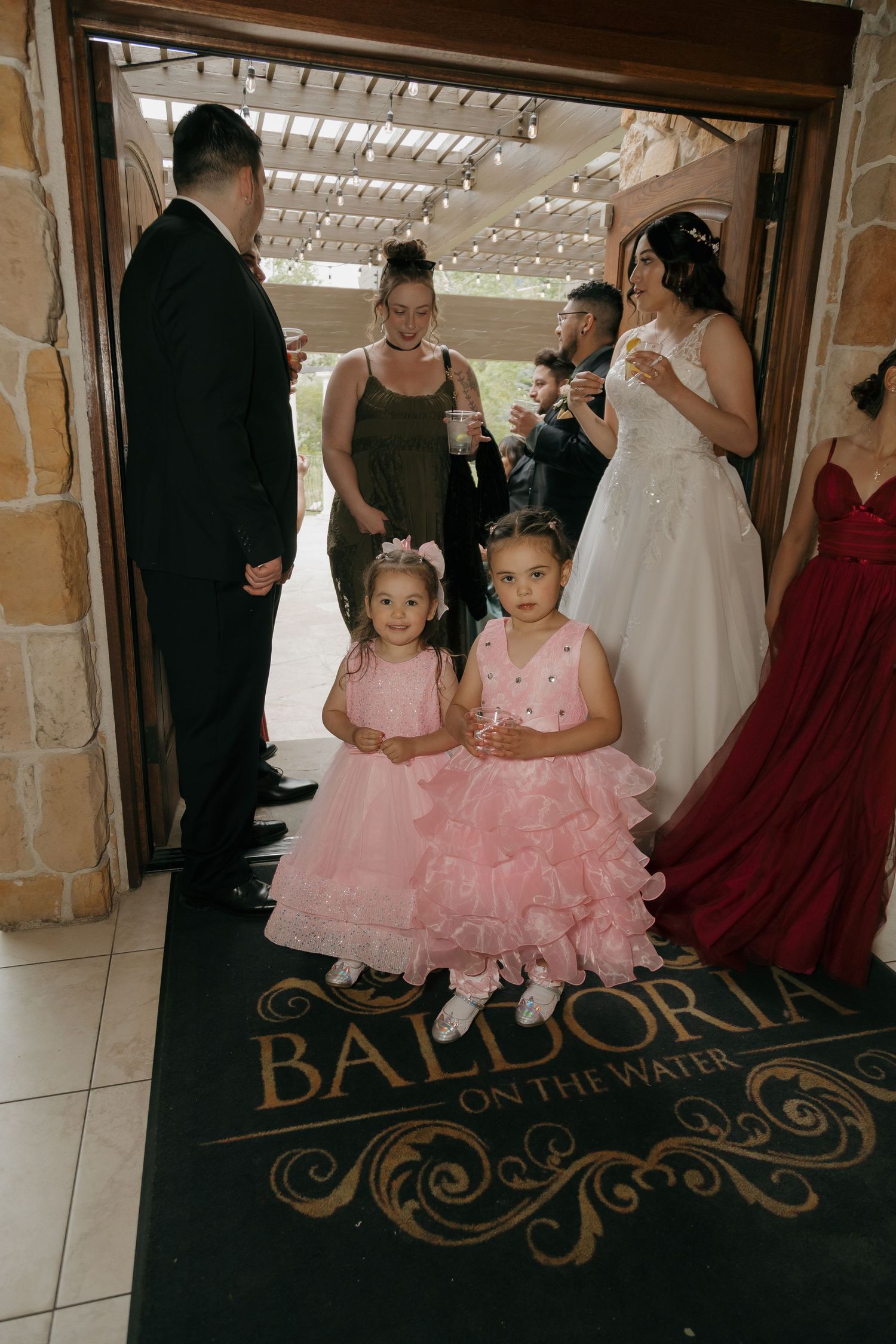 Two flower girls in pink dresses stand at the entrance of Baldoria on the Water wedding venue.