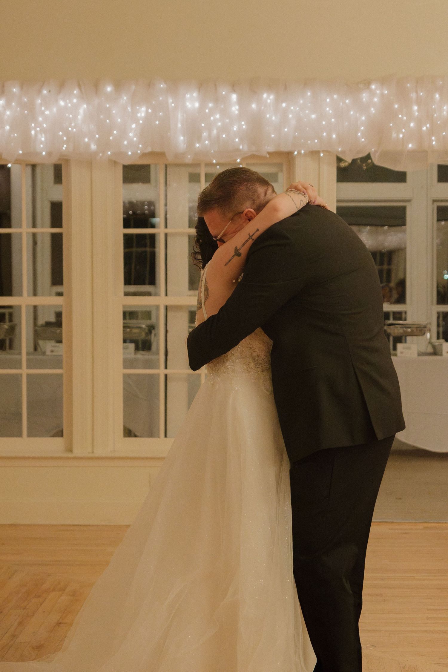 A couple shares their first dance as newlyweds in an elegant venue with twinkling lights in the background.