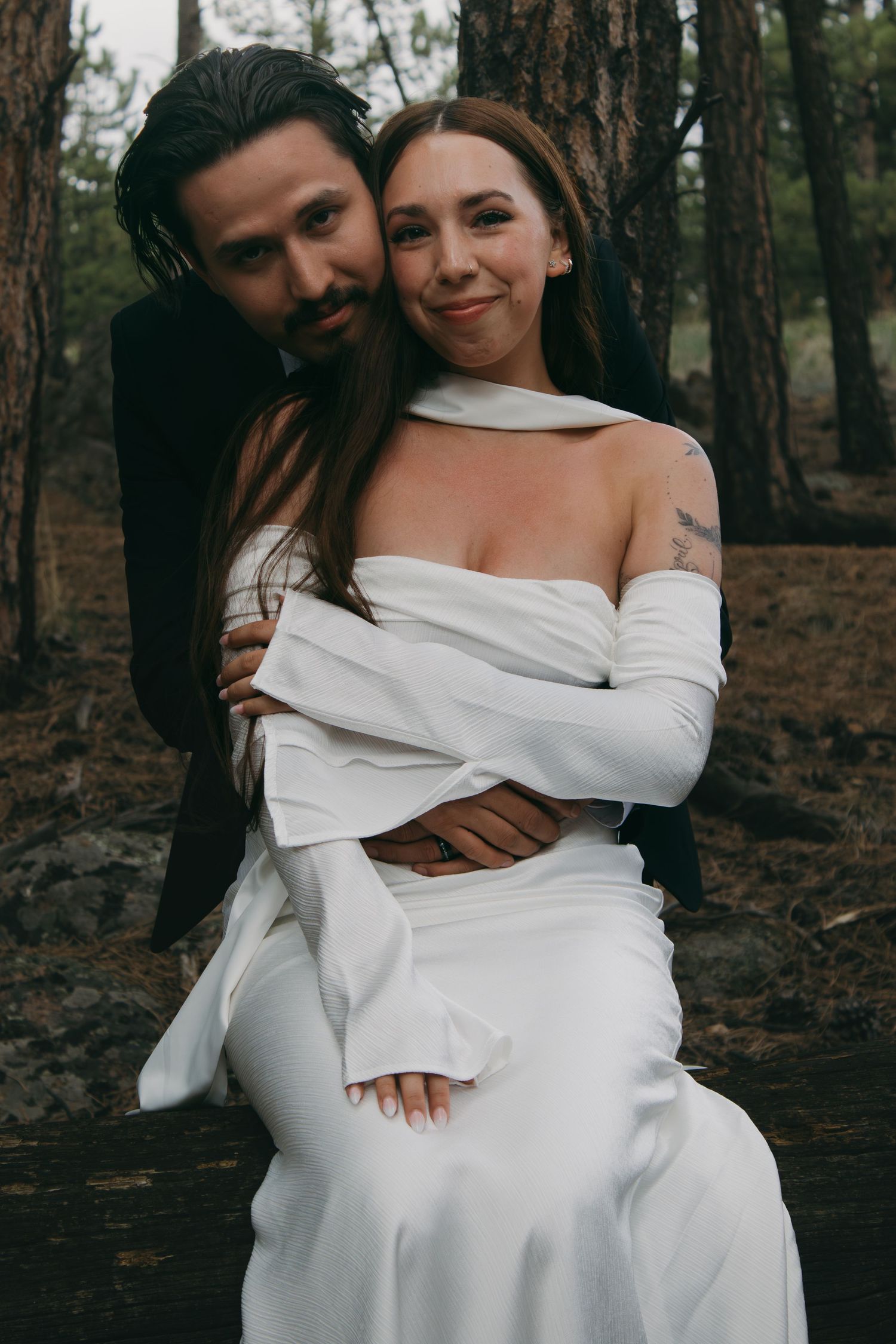 A couple embraces intimately in a forest setting wearing white clothing in a series of romantic photographs.