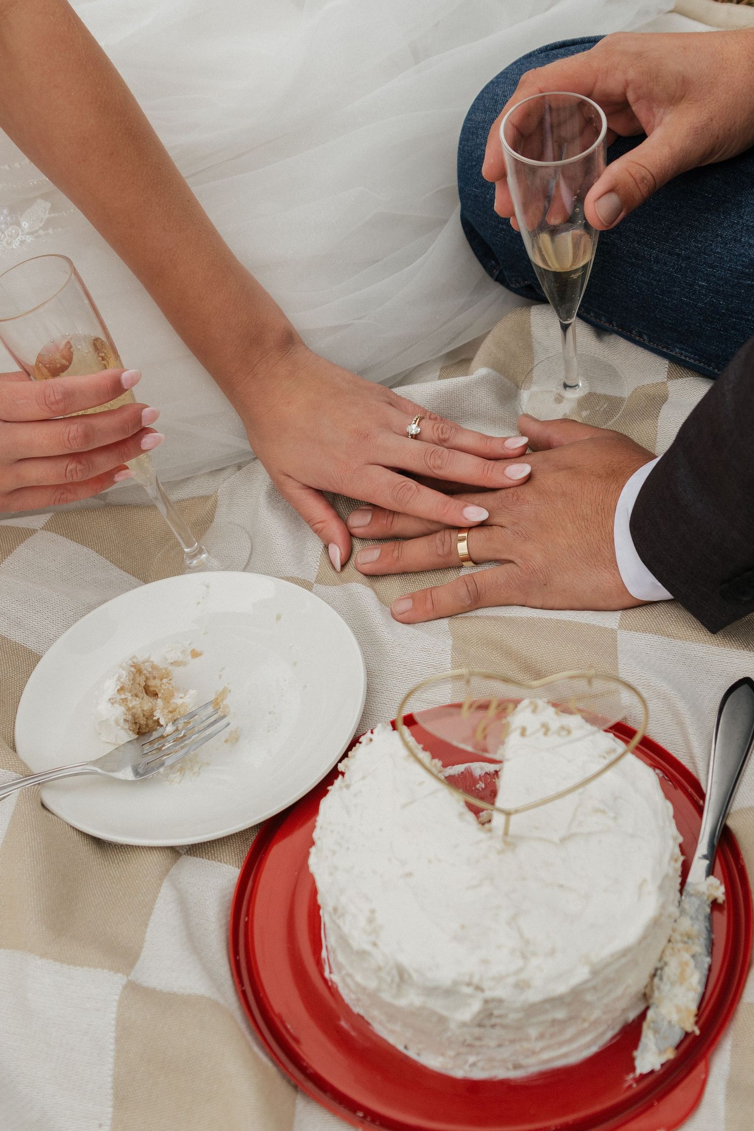 Close-up of hands cutting into a white wedding cake on red plates during a celebration.