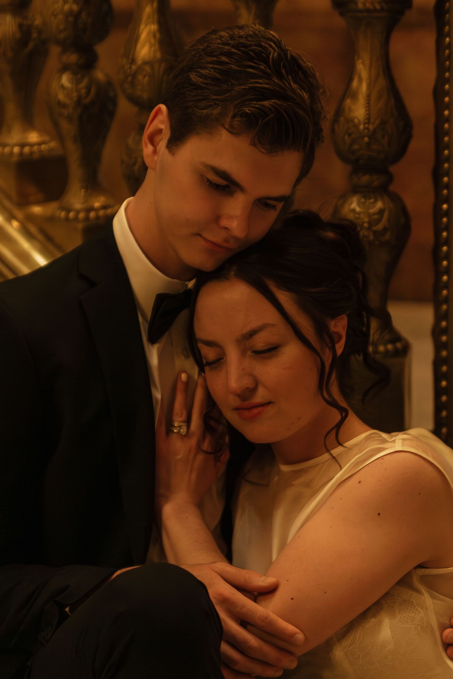 A warmly lit wedding portrait showing a tender embrace against ornate golden decor.