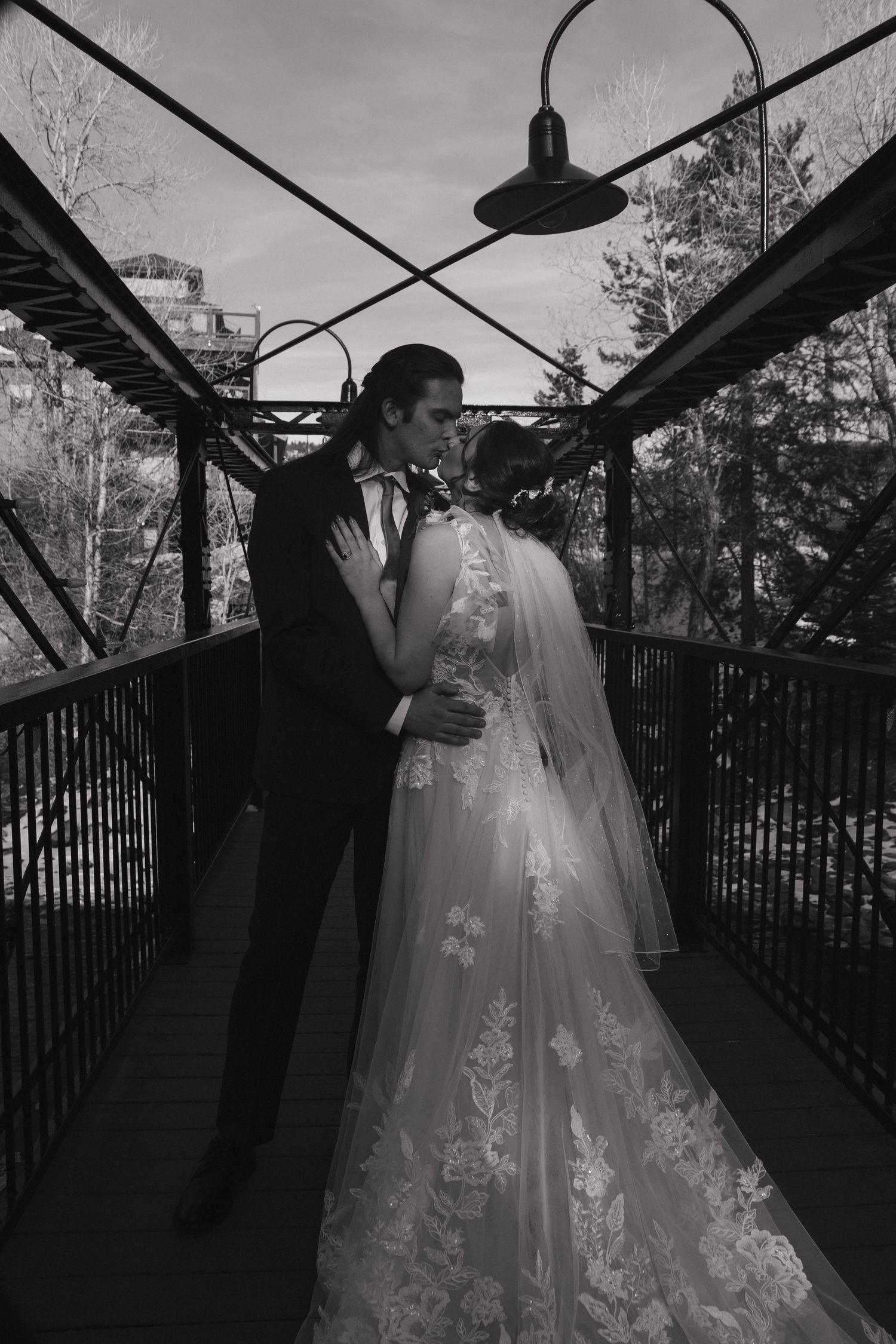 A romantic wedding couple shares intimate moments in black and white on a covered bridge with iron railings.