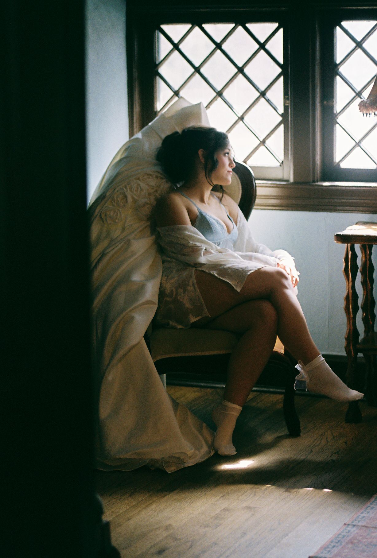 A series of moody window-lit photographs showing someone in a white dress sitting contemplatively by a latticed window.