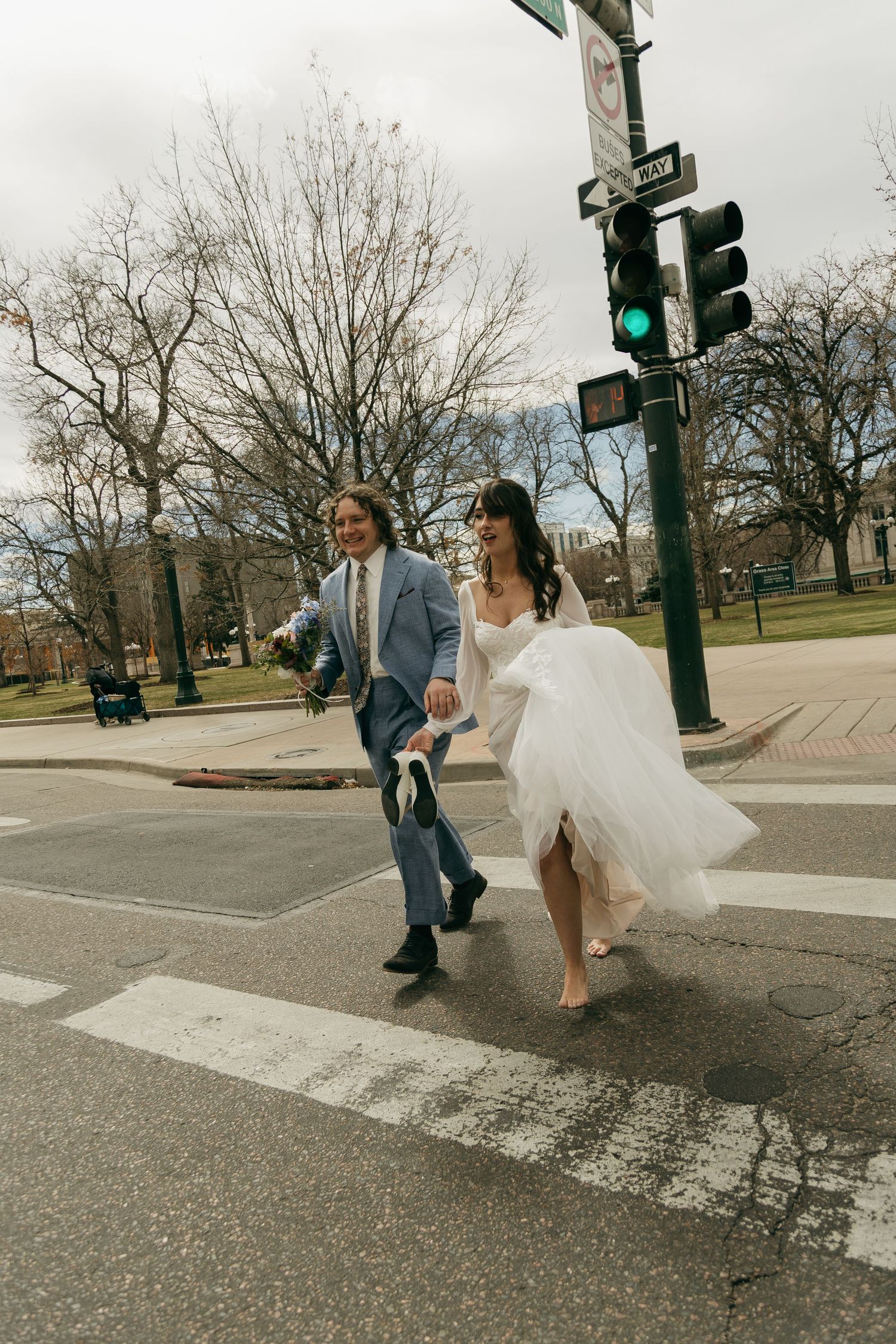 A wedding party playfully crossing a crosswalk with flowing white dress billowing in the wind.