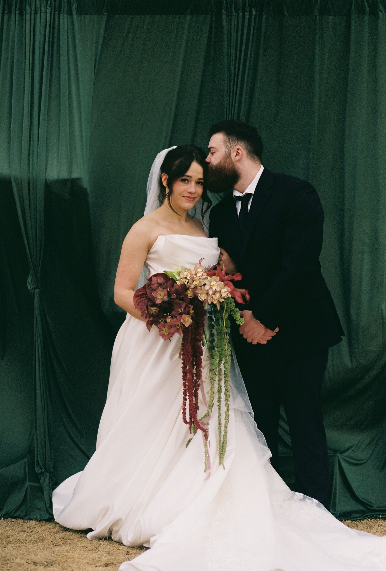 A couple shares an intimate moment against a dark backdrop with cascading floral bouquet.