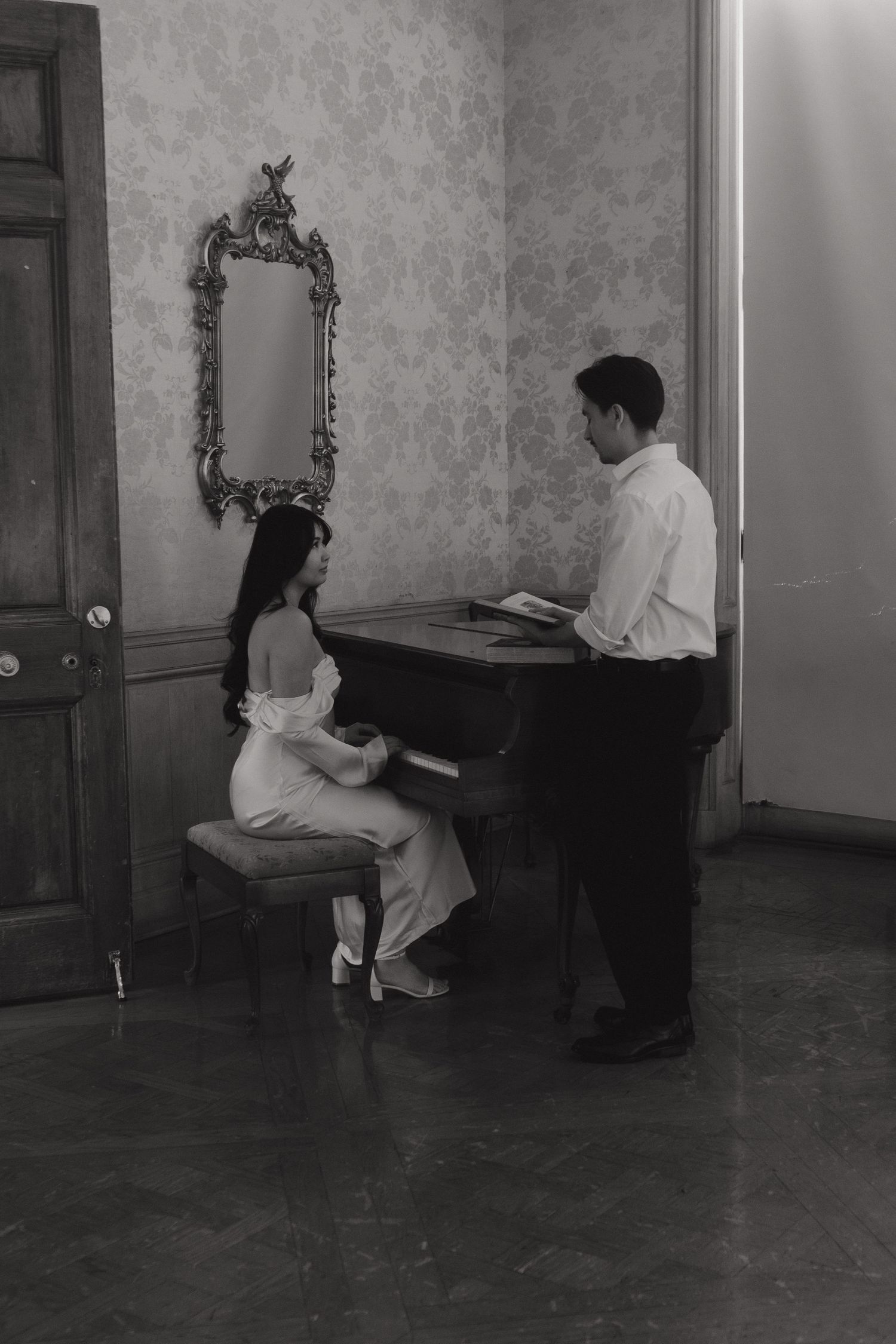 Couple shares tender moment at piano in elegant room with ornate mirror.