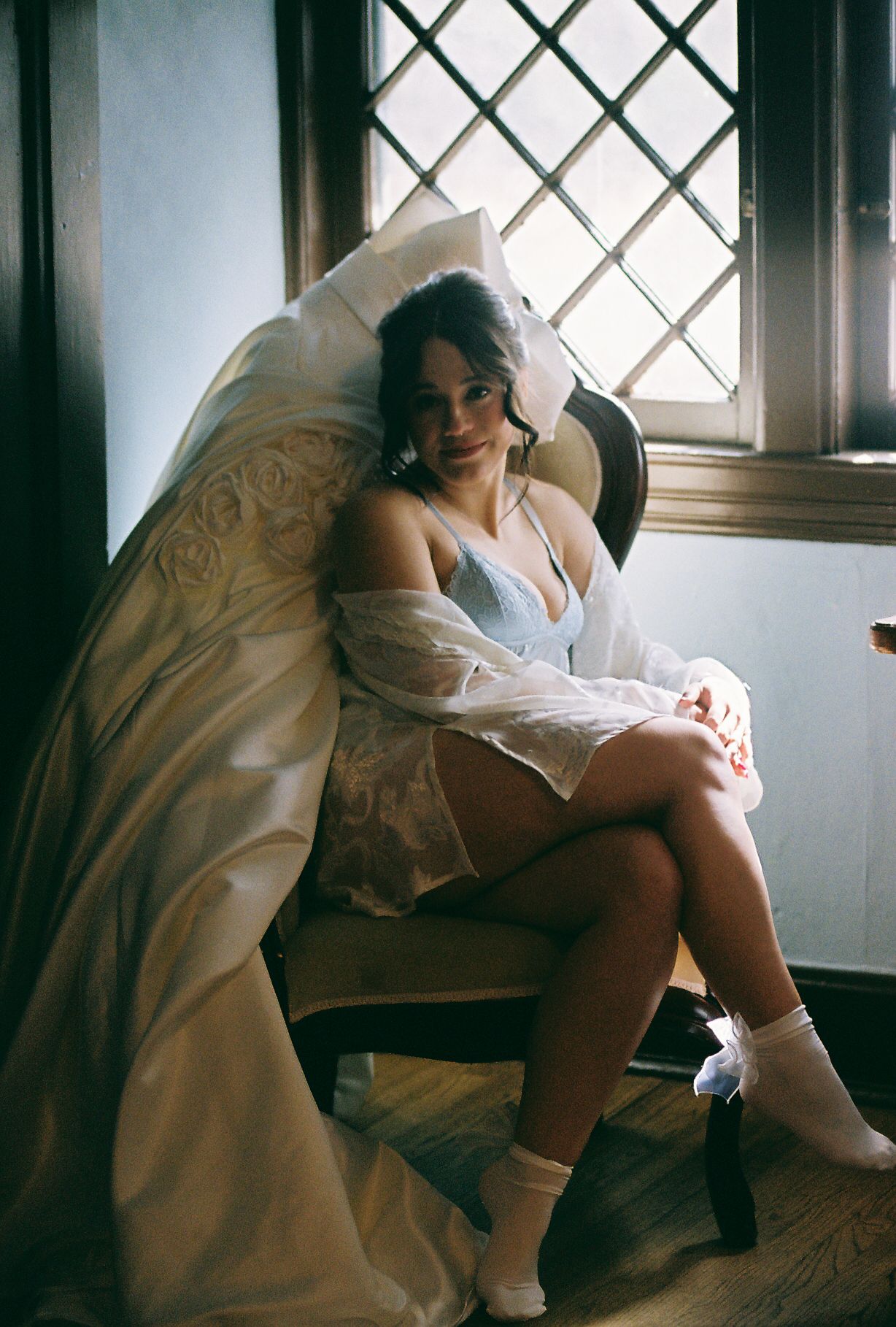 A person in a white dress sits contemplatively by a window with diamond-patterned panes.