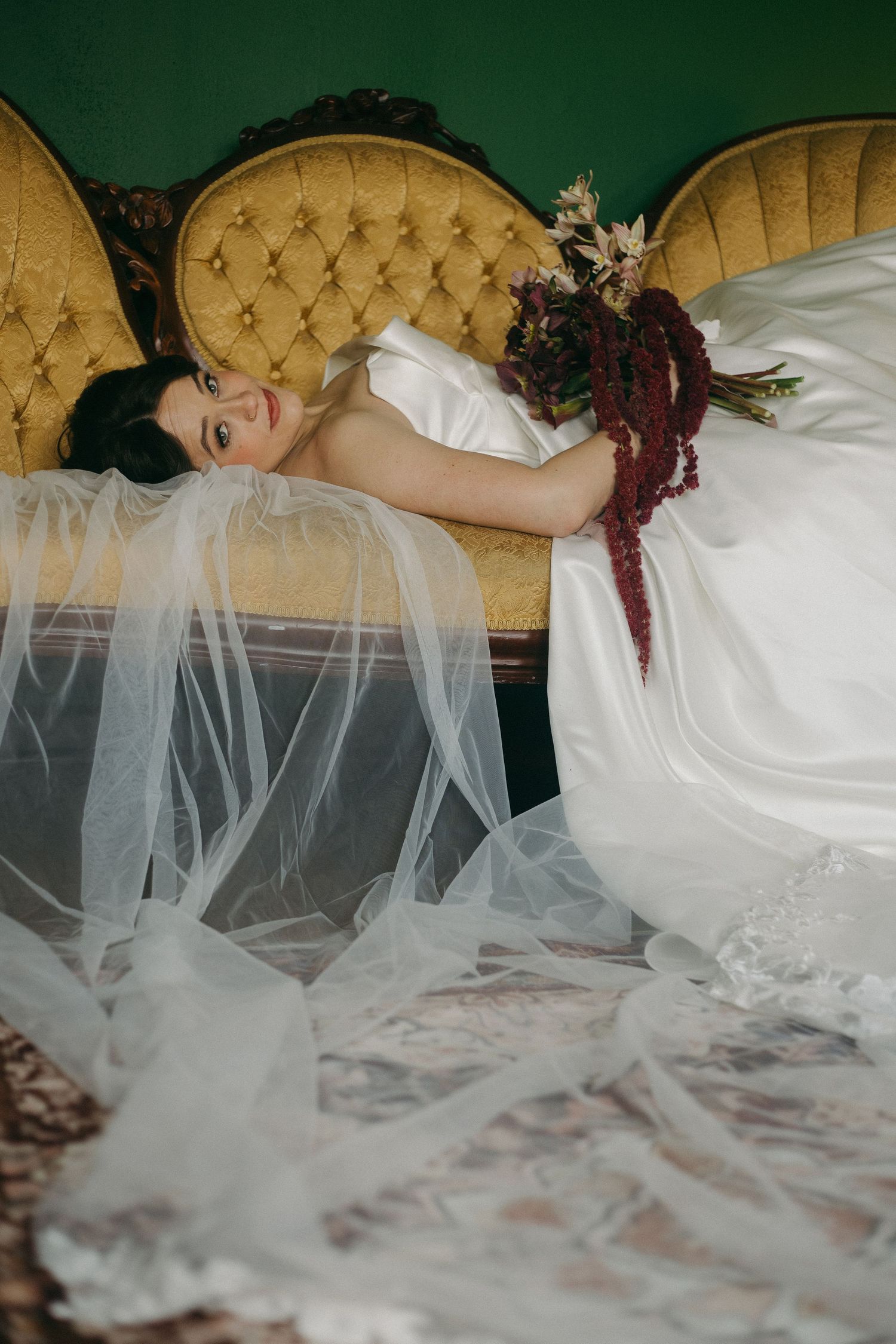 A flowing white wedding dress with delicate tulle veil draped across an elegant couch.