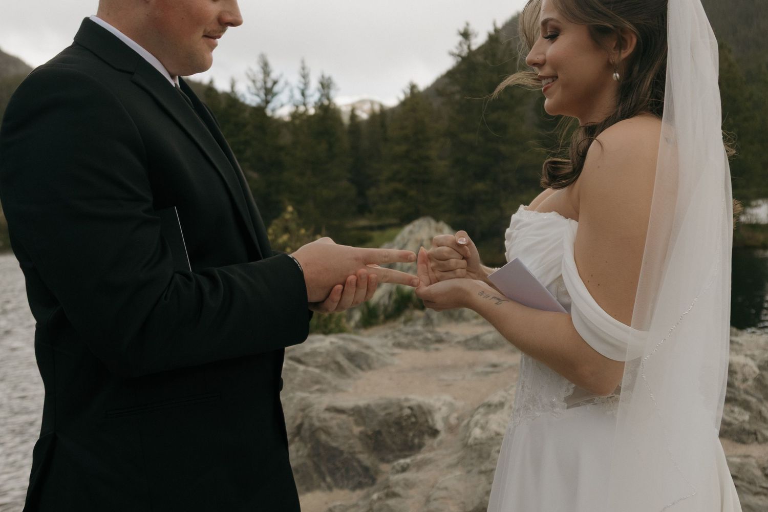 Bride and groom exchanging rings outdoors with mountain forest backdrop during intimate elopement ceremony.