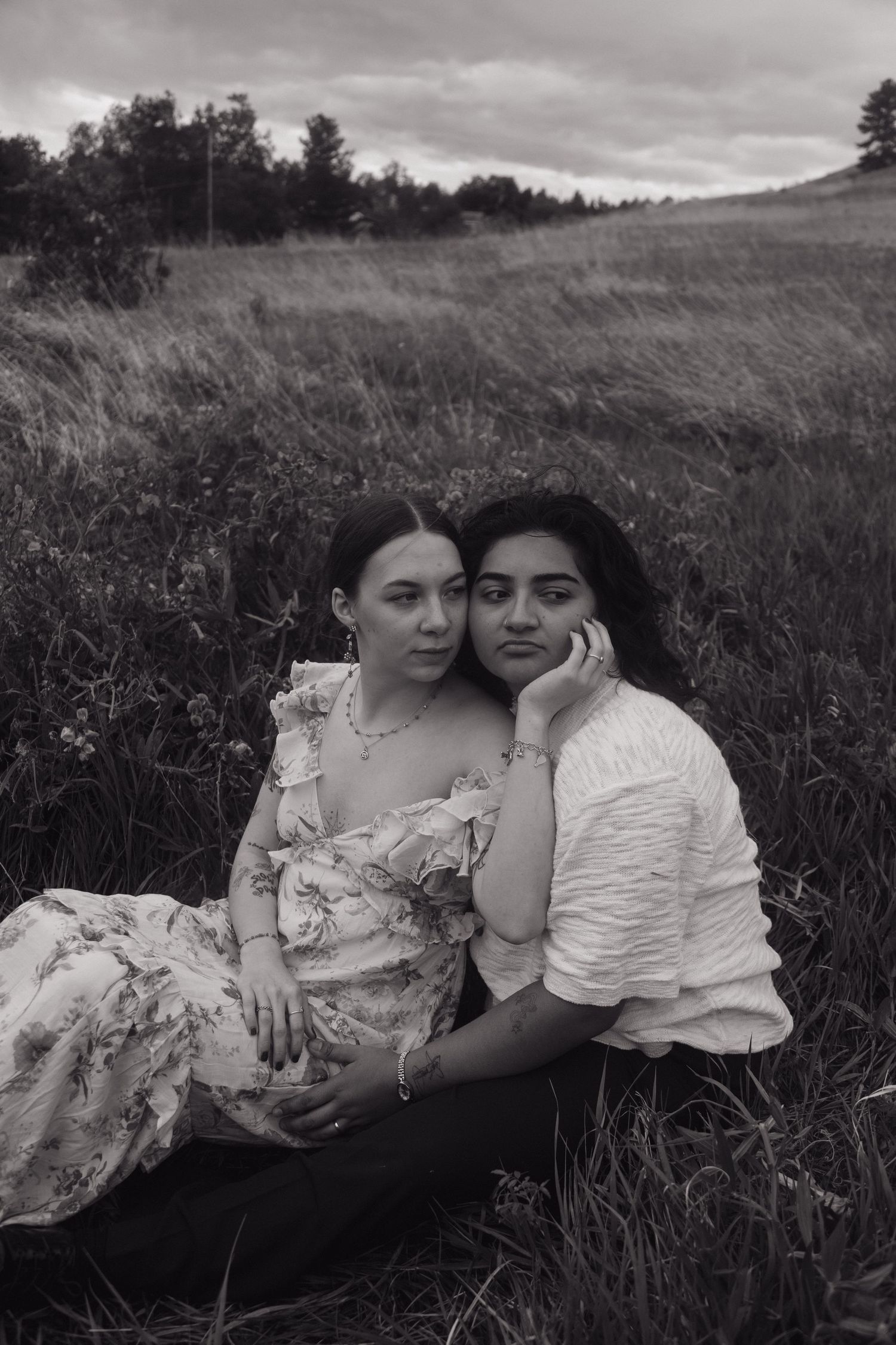 Black and white portrait of two women sitting closely together in a lush meadow grass field.