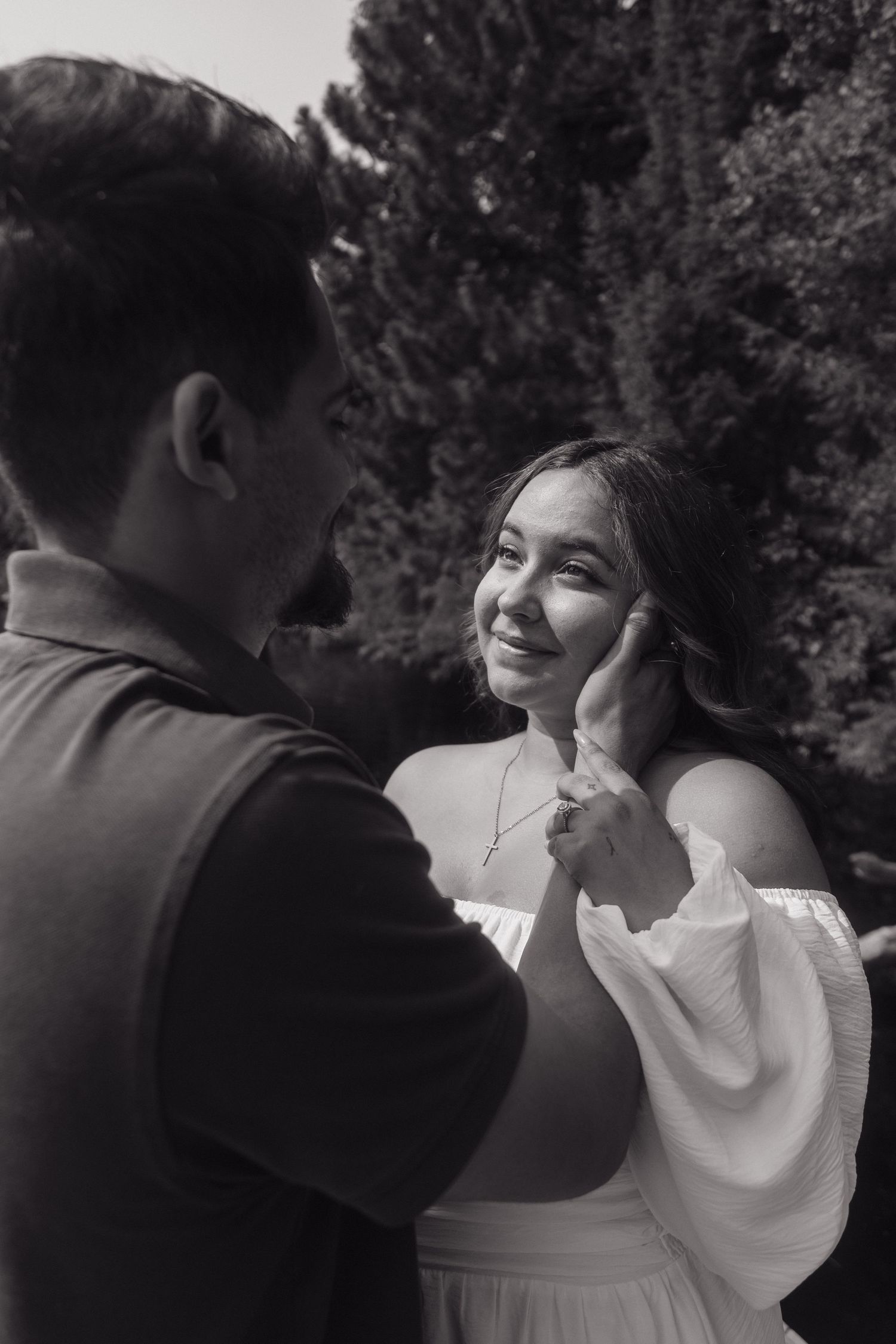 Black and white photo of a couple sharing a tender moment outdoors, man gently touching womans face as she smiles.