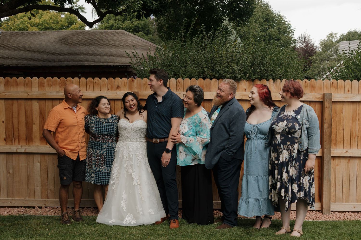 Outdoor wedding scene with figures gathered in a backyard garden setting beneath string lights at dusk.