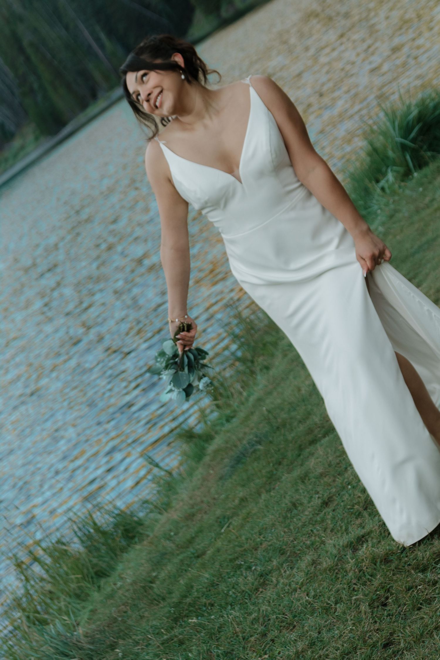Elegant bridal portrait showing details of a sleek white wedding dress near a lake.