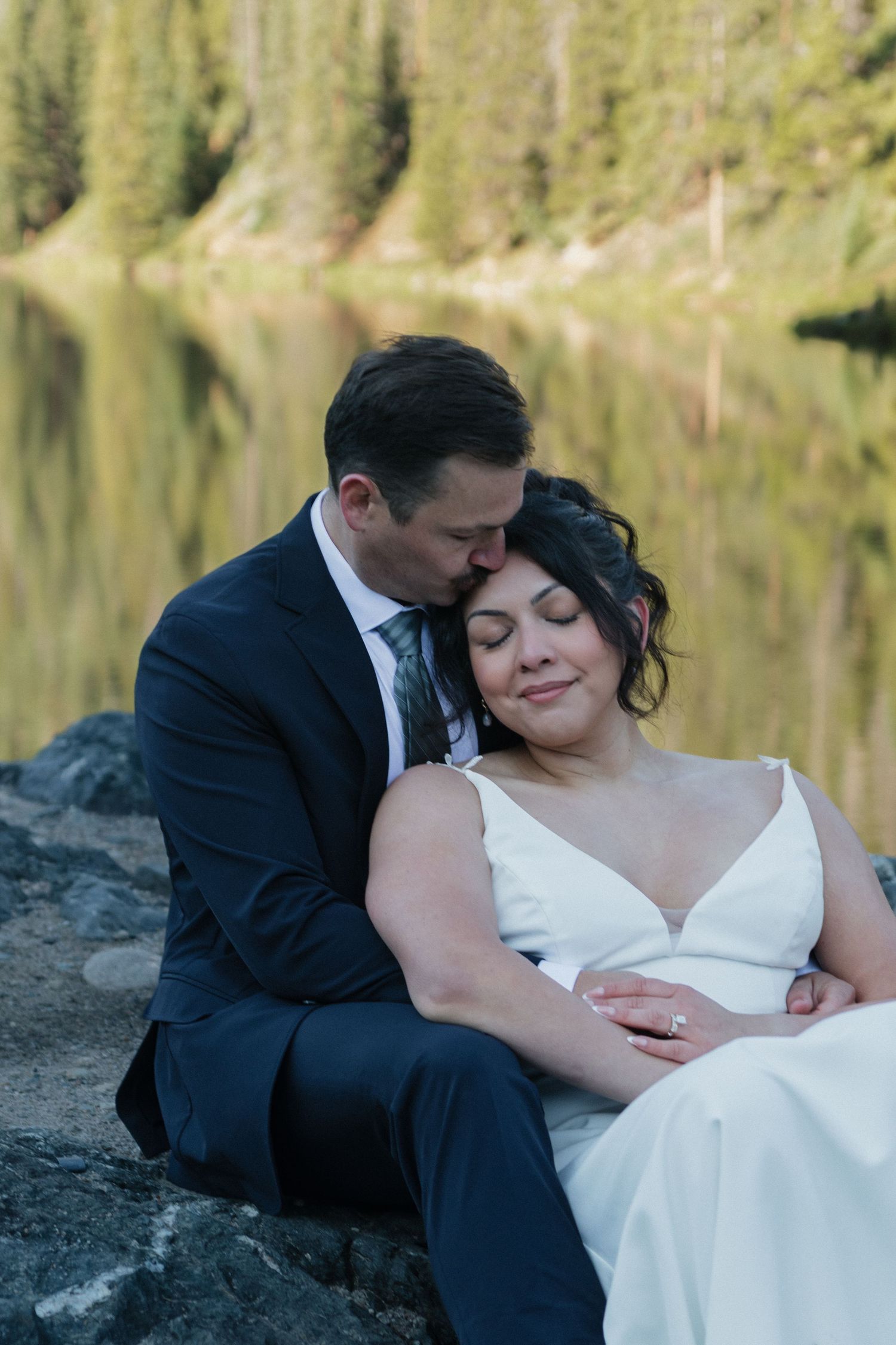 Romantic wedding couple resting together by a serene lake during sunset.