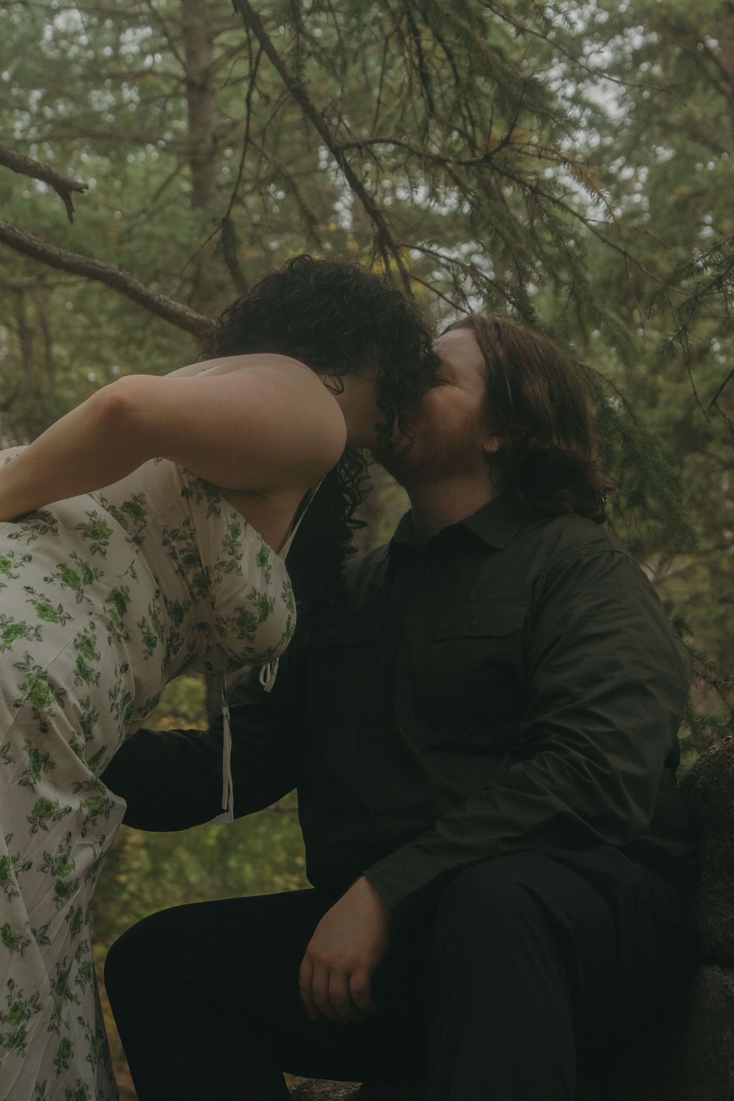 Two figures in dark and light clothing embrace in an intimate dance pose among trees in a forest setting.