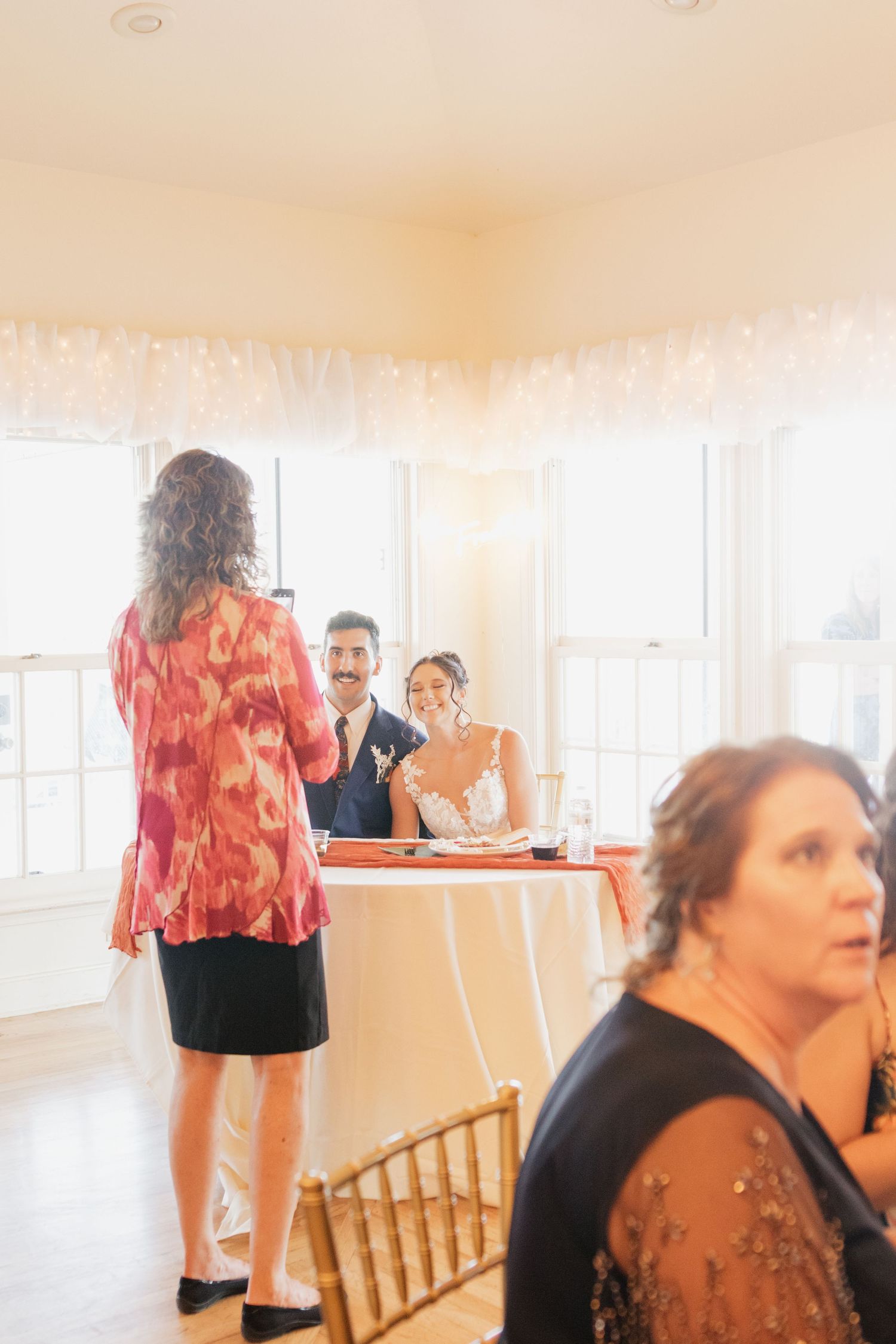 Wedding reception room with bright windows and guests in casual attire.