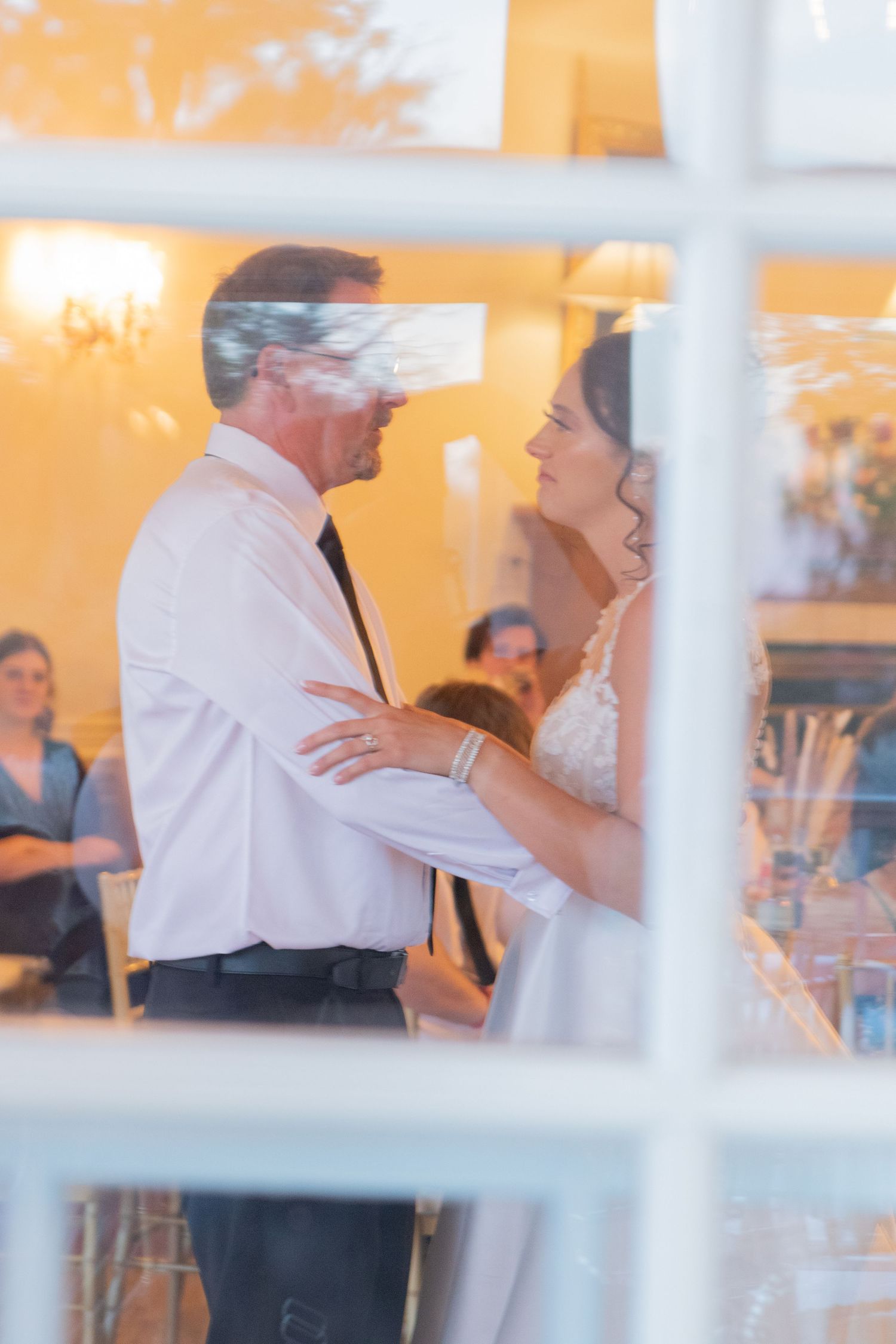 Dancing couples seen through window panes at evening wedding reception.