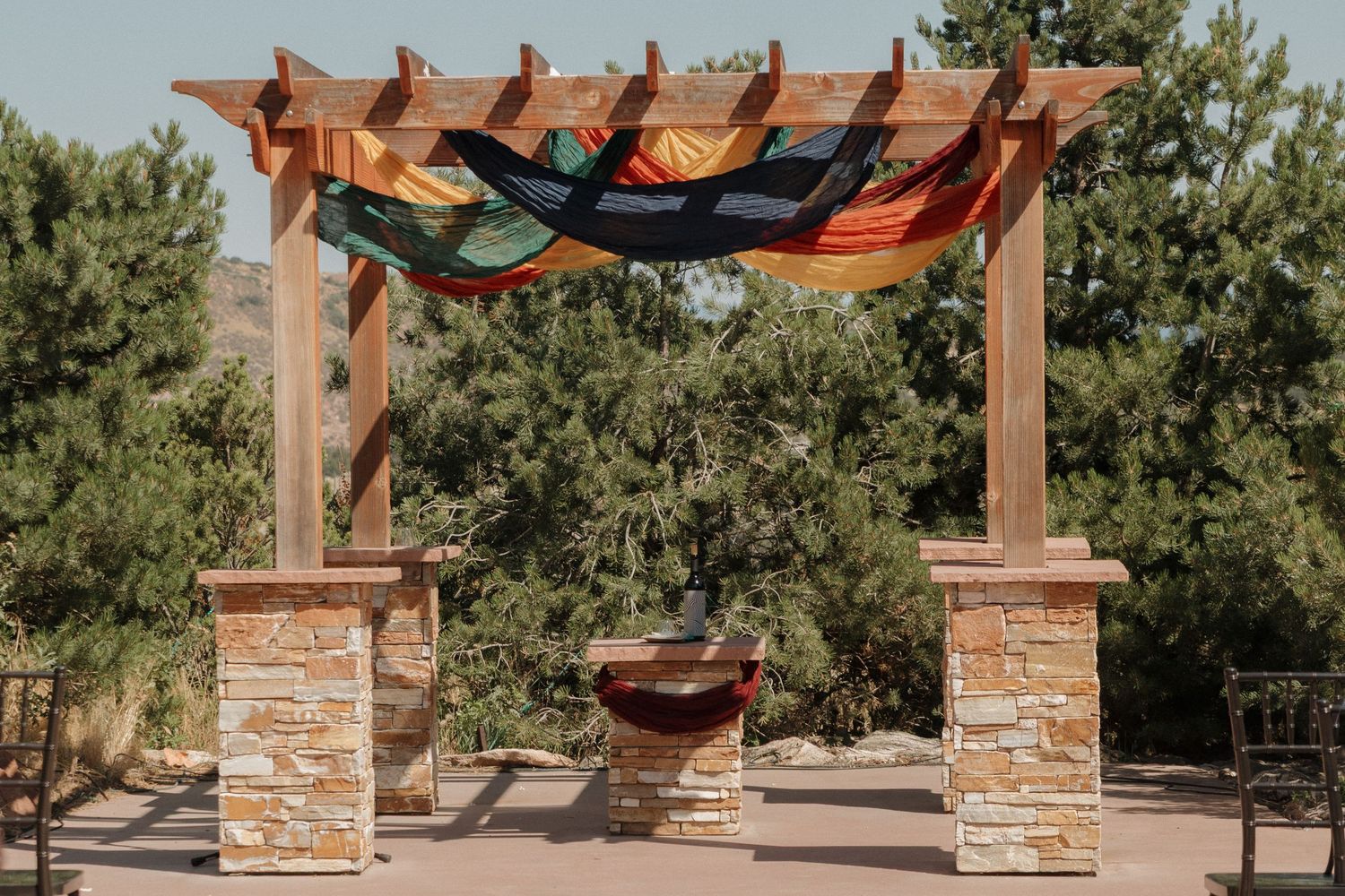Outdoor wedding venue with stone columns and wooden pergola against a clear blue sky.