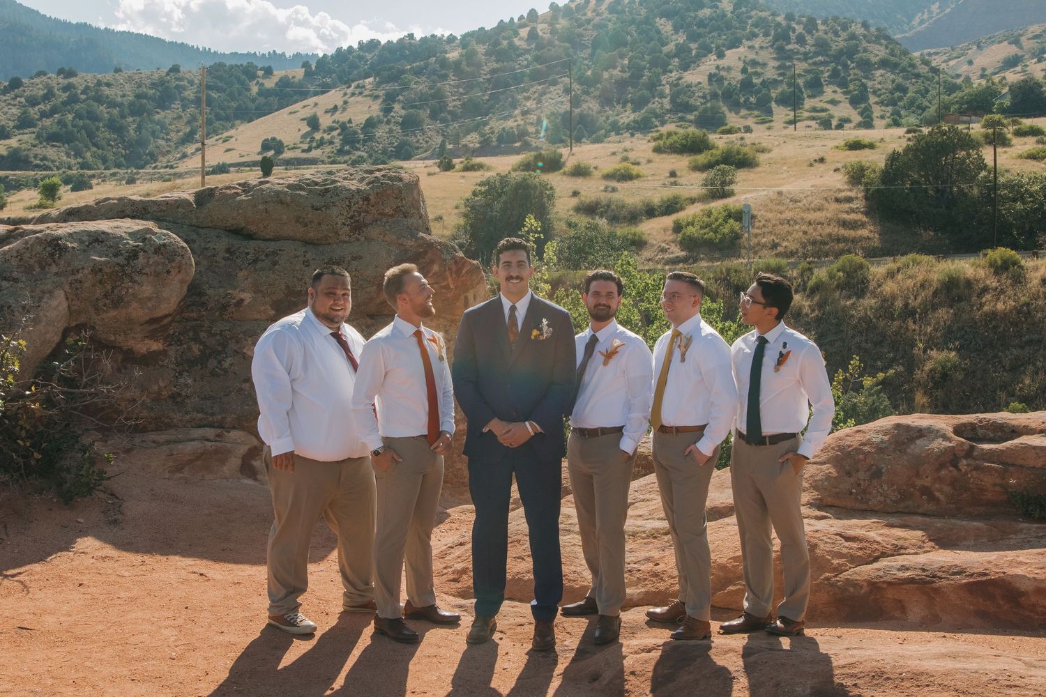 Wedding party posing on rocky terrain with mountain vista in background.
