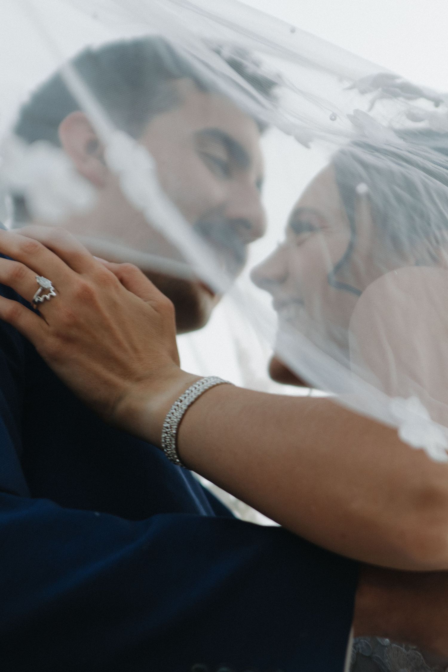 Close-up detail shot of hands and veil during intimate wedding moment.