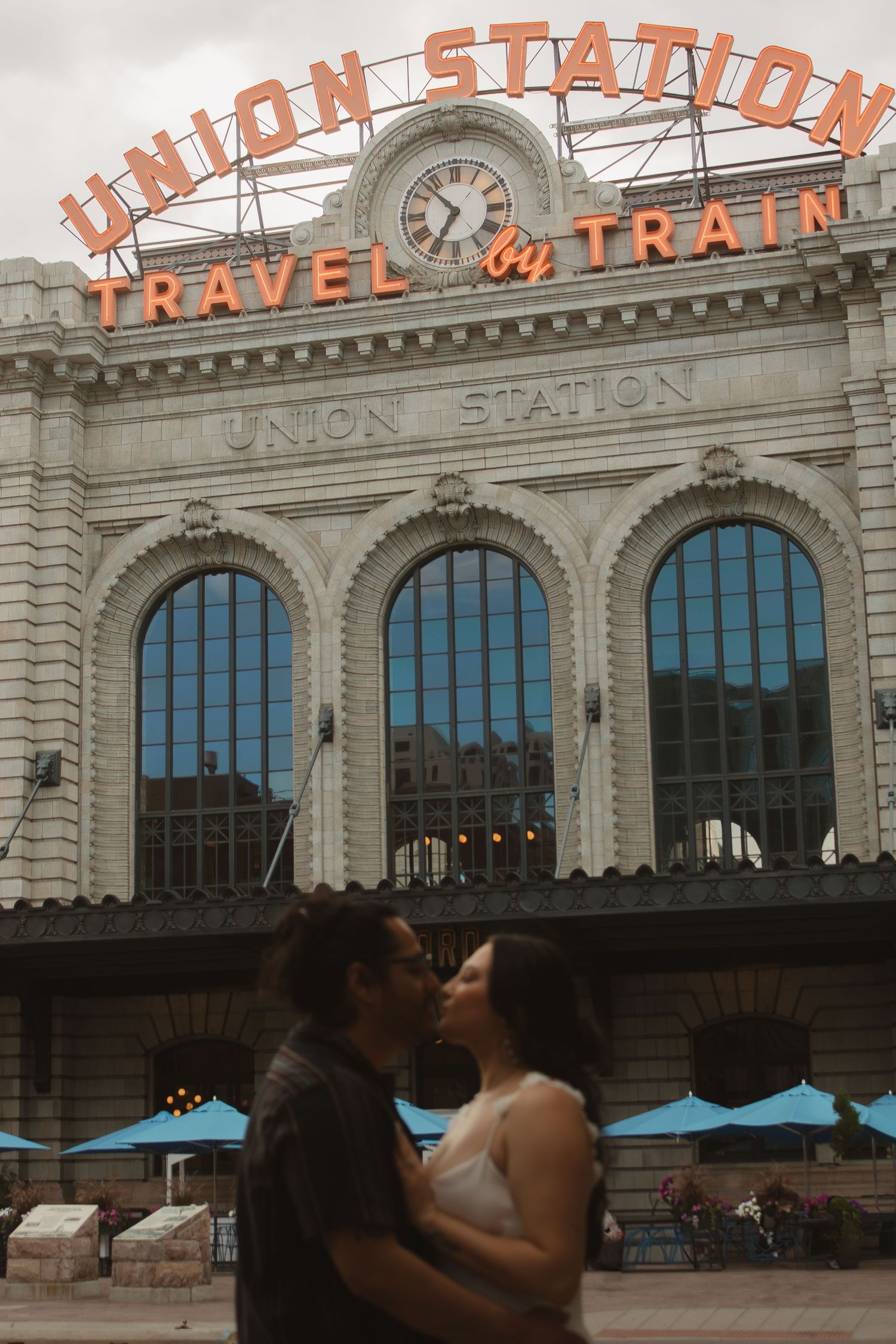 A romantic moment in front of the historic Union Station Travel by Train building with arched windows and neon signage.