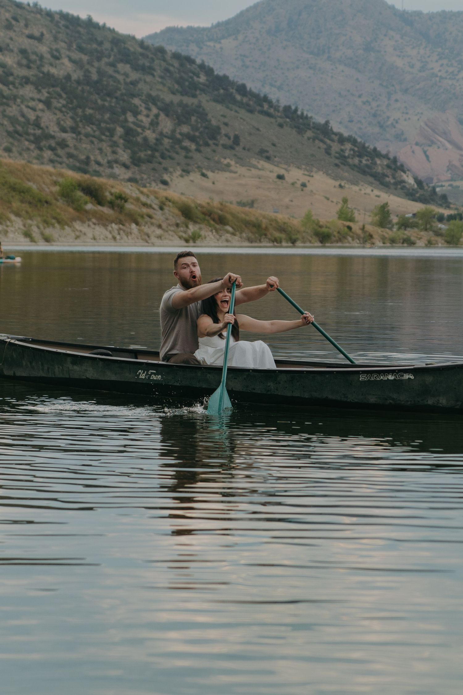A couple enjoys a peaceful canoe ride on a lake surrounded by mountain scenery.
