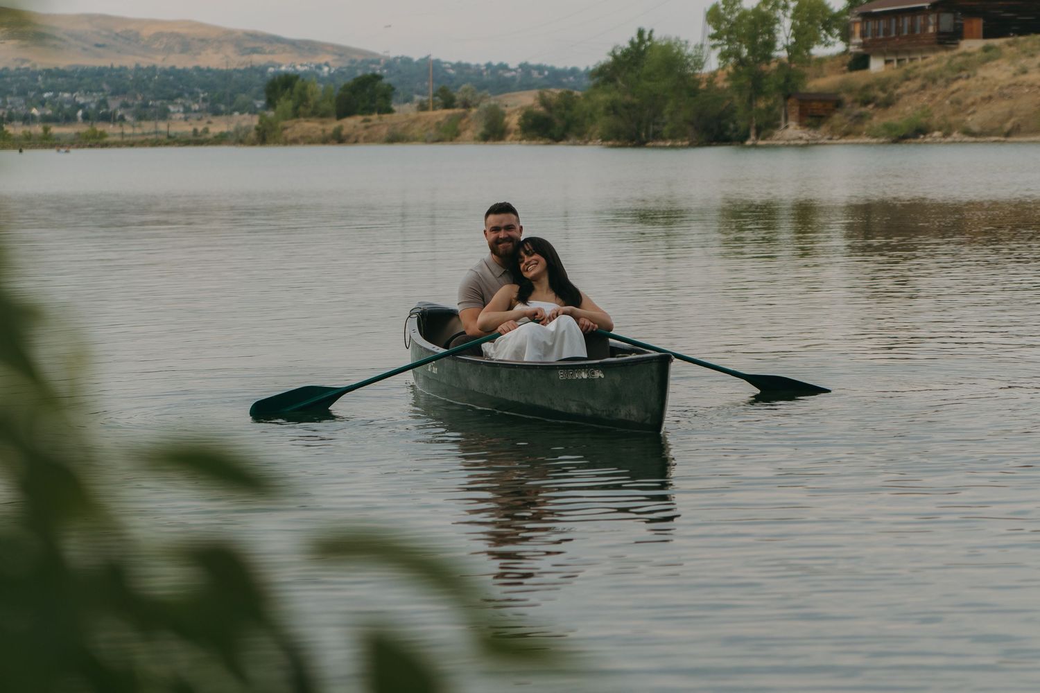A small boat glides across a scenic lake with mountains and trees in the background.