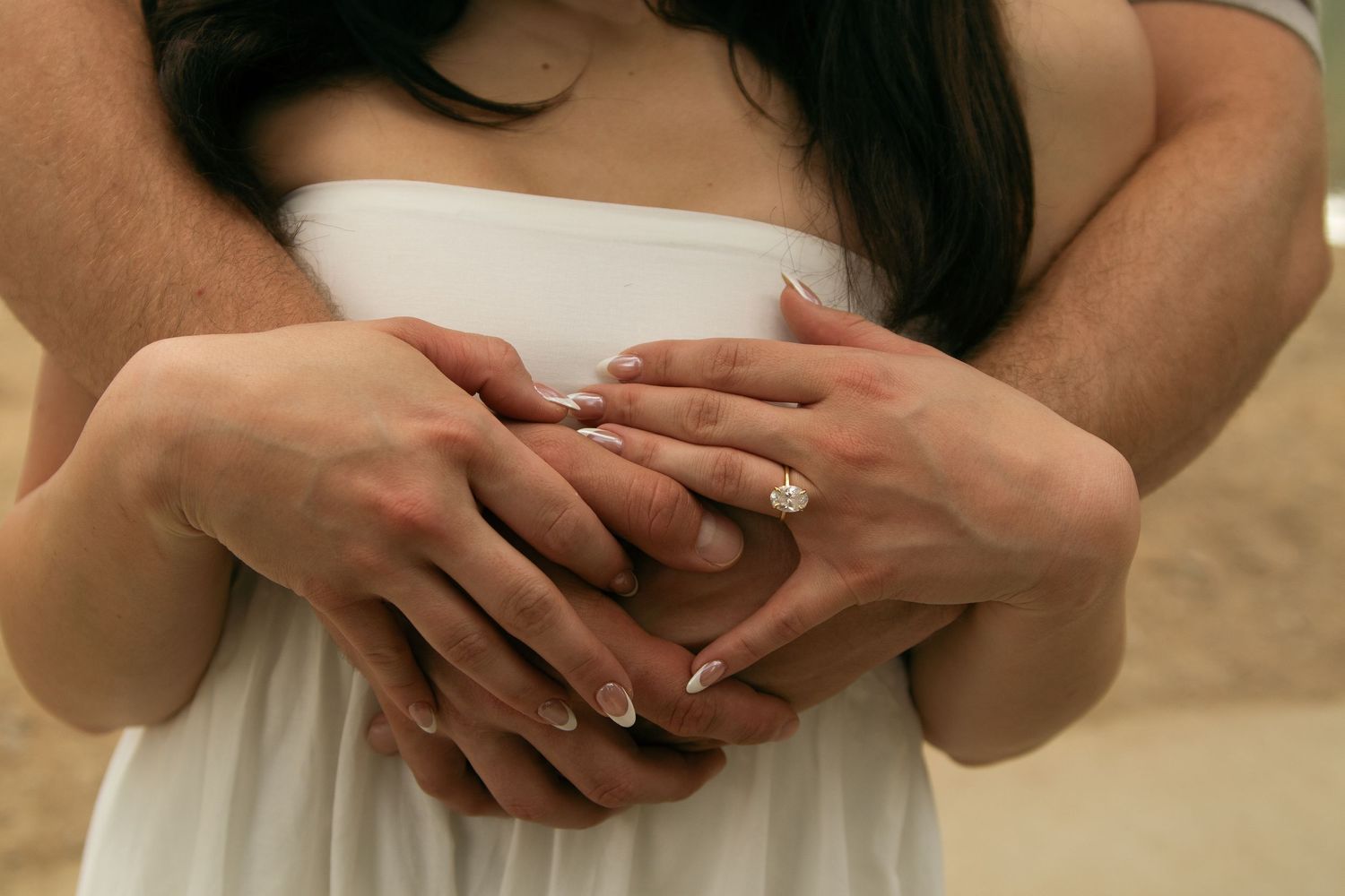 Close-up shot of hands tenderly touching and intertwining against a light background.