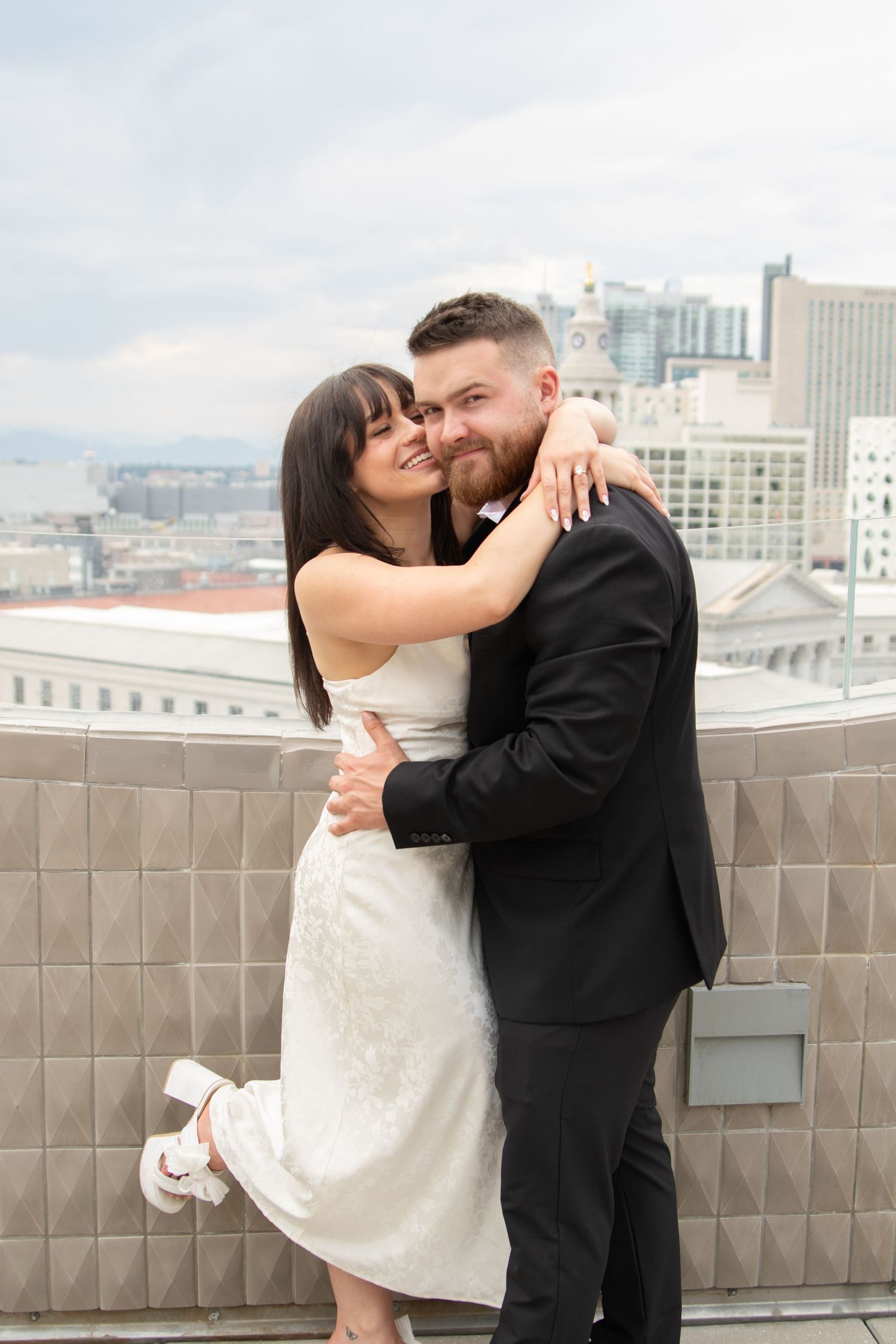 A couple embraces on an urban rooftop with city buildings in the background.