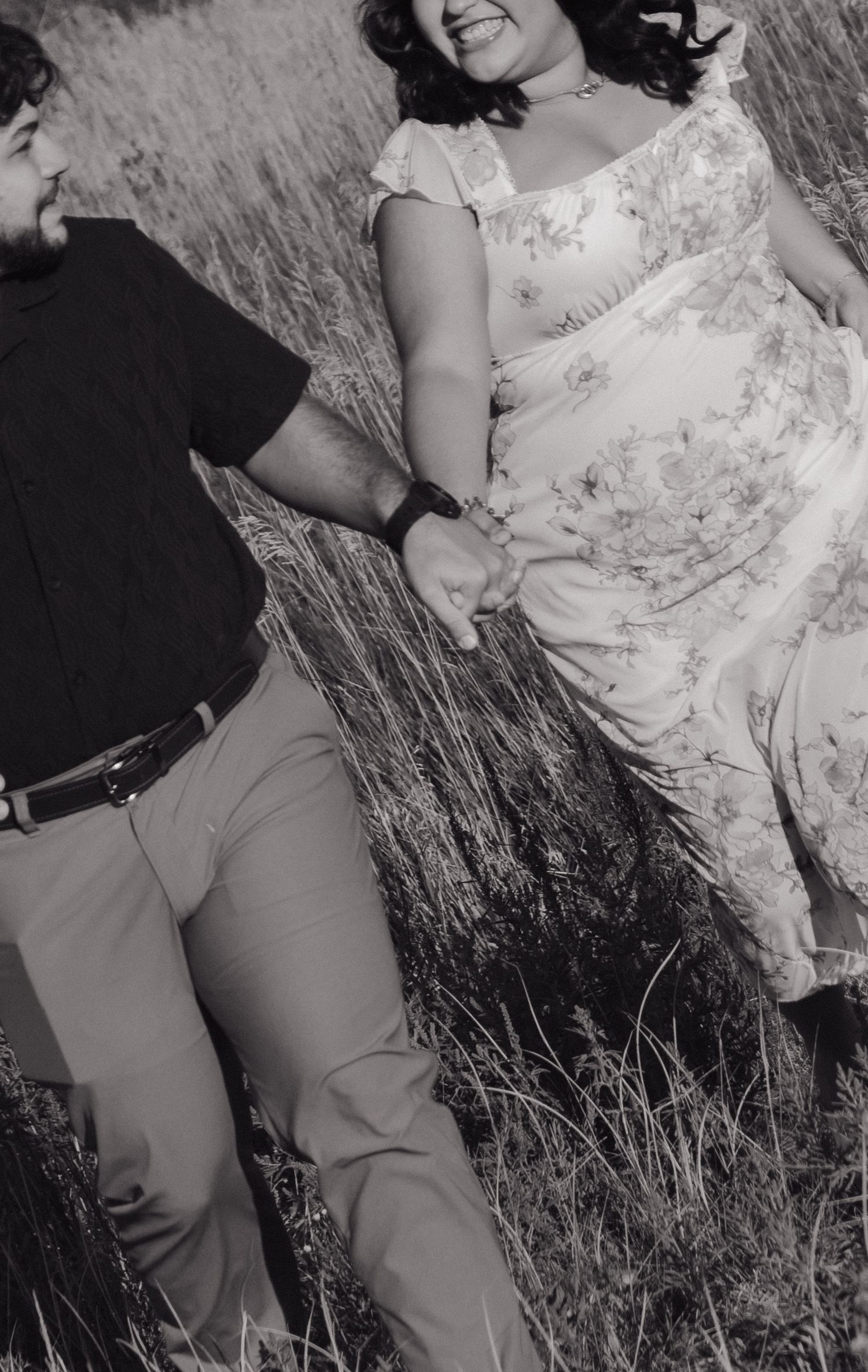 A black and white photo captures a couple in a field of tall grass.