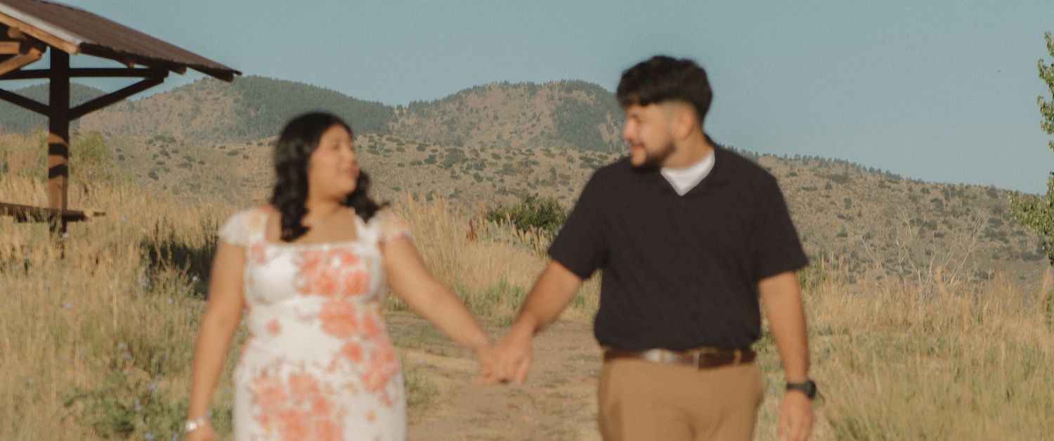 A couple holds hands while walking together in front of desert mountains.