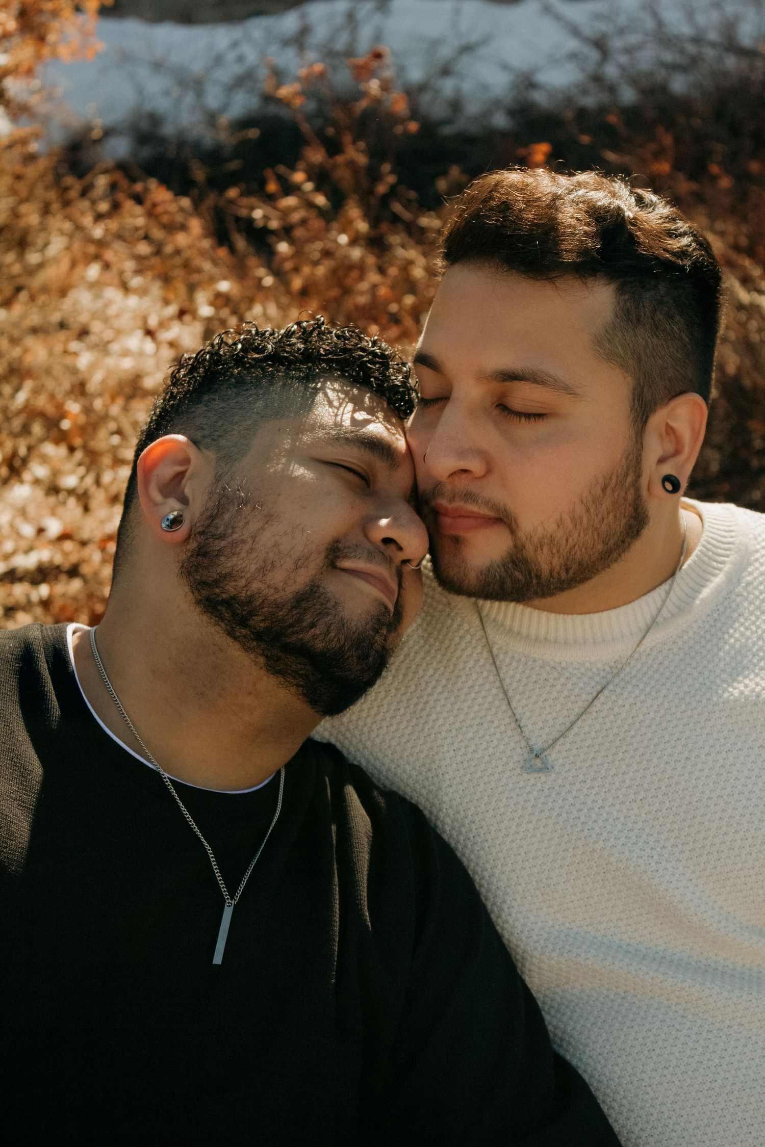 A tender moment between a couple wearing black and white sweaters against an autumn background.